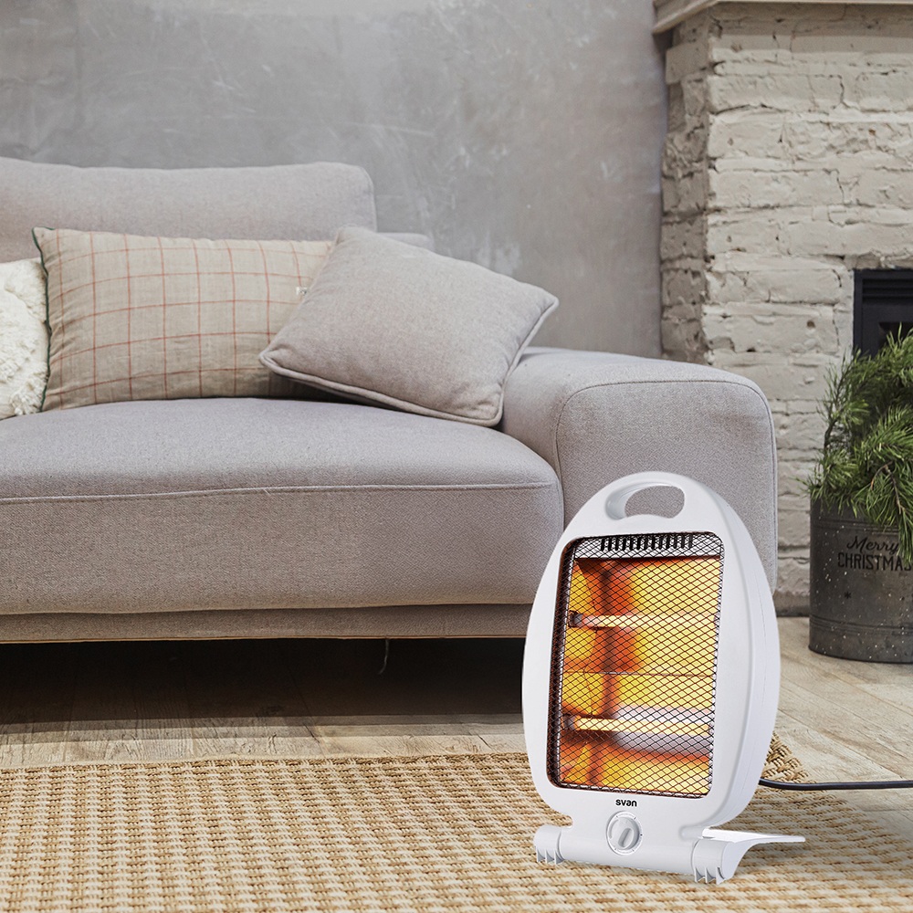 Un calefactor eléctrico blanco está sobre una alfombra frente a un sofá gris. Detrás del sofá hay una pared gris y una chimenea.