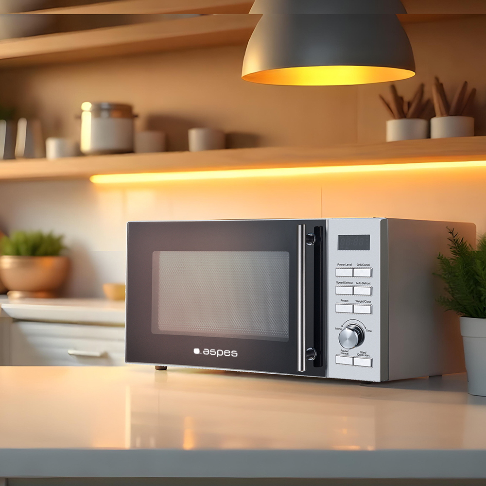 Kuchenka mikrofalowa na białym blacie. Powyżej lampa i półki z przyborami kuchennymi. Mała roślina po prawej.
