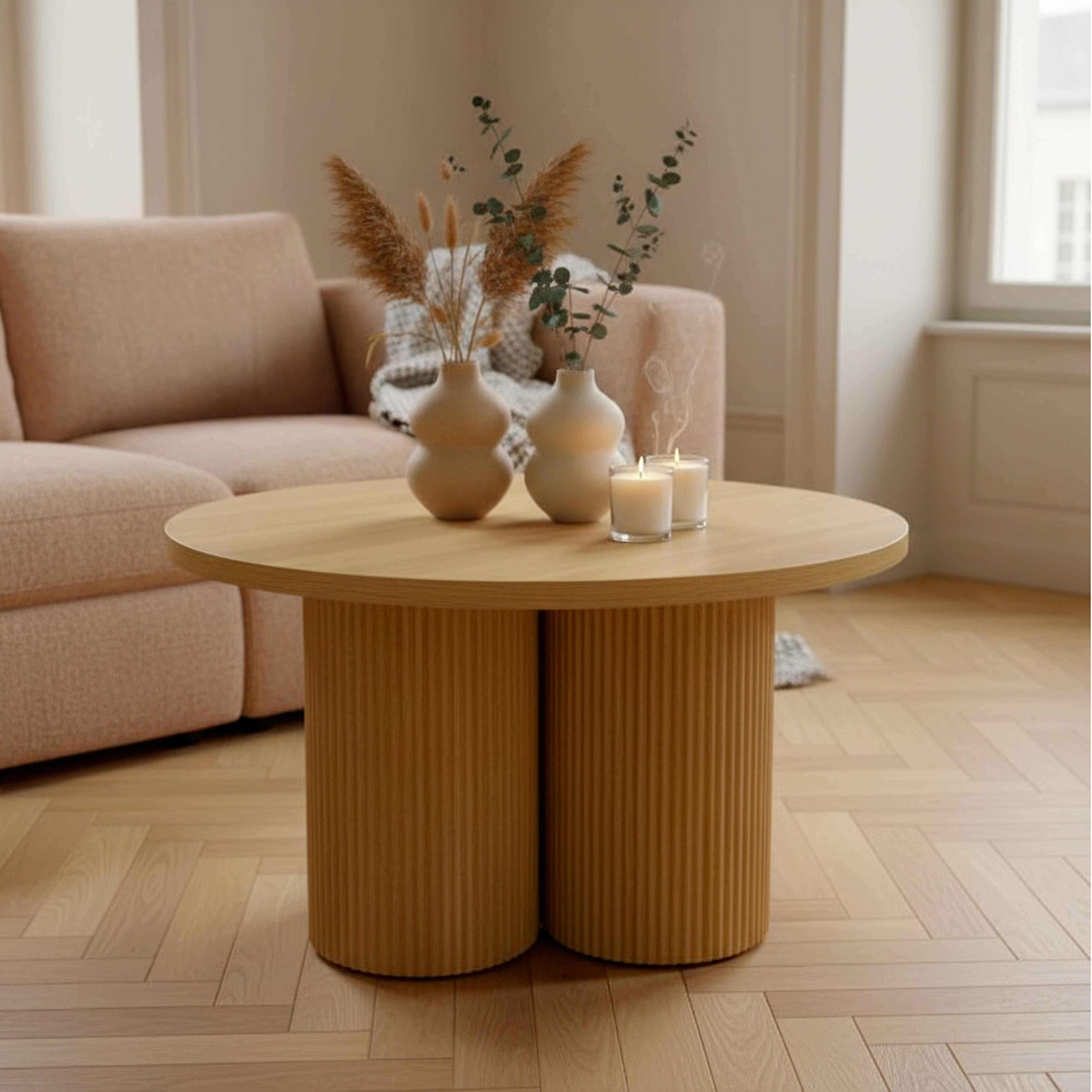 Ein runder Holztisch mit zwei zylindrischen Beinen. Vasen, Kerzen und ein Sofa im Hintergrund.