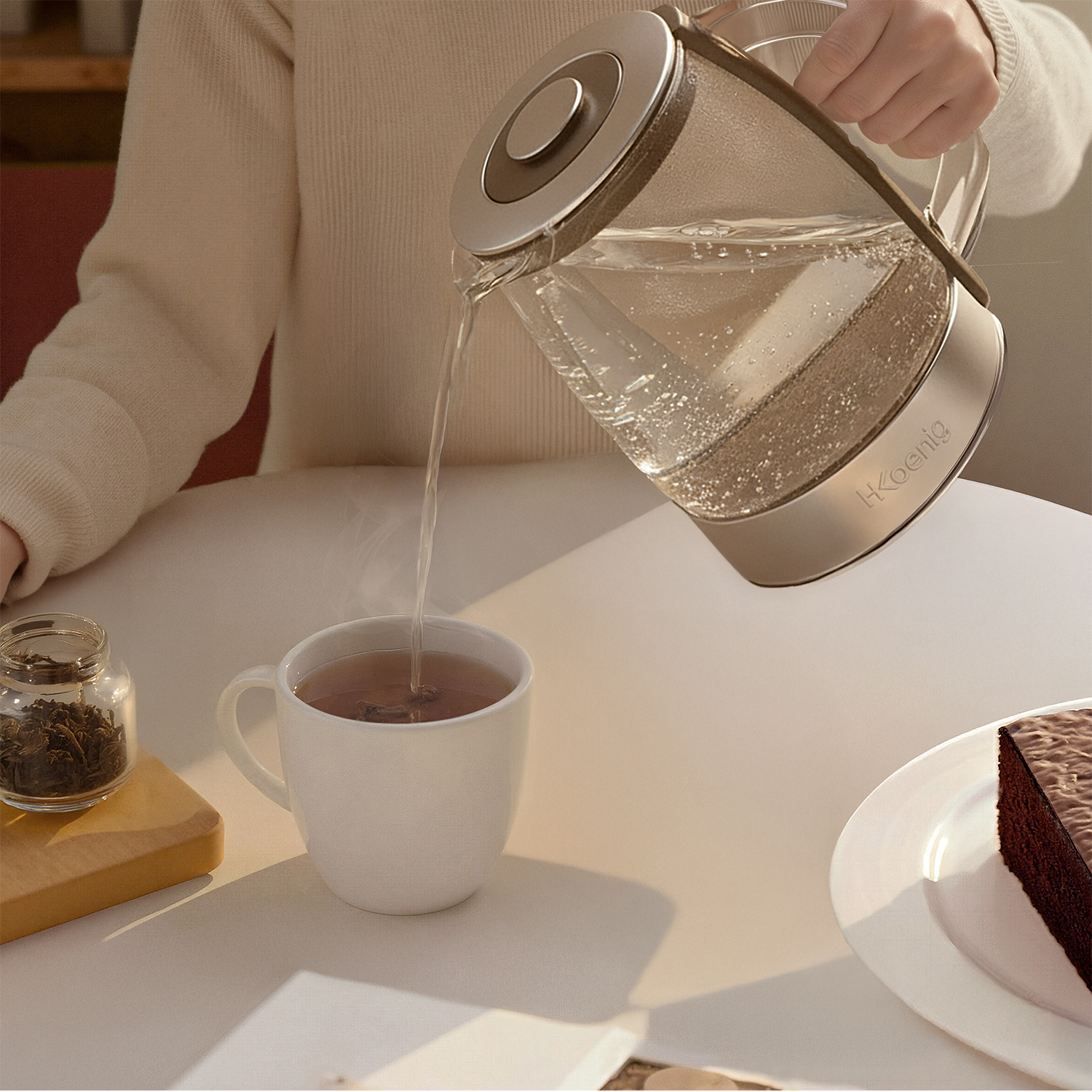 Una persona versa acqua calda da un bollitore di vetro in una tazza bianca. Foglie di tè e torta sul tavolo.