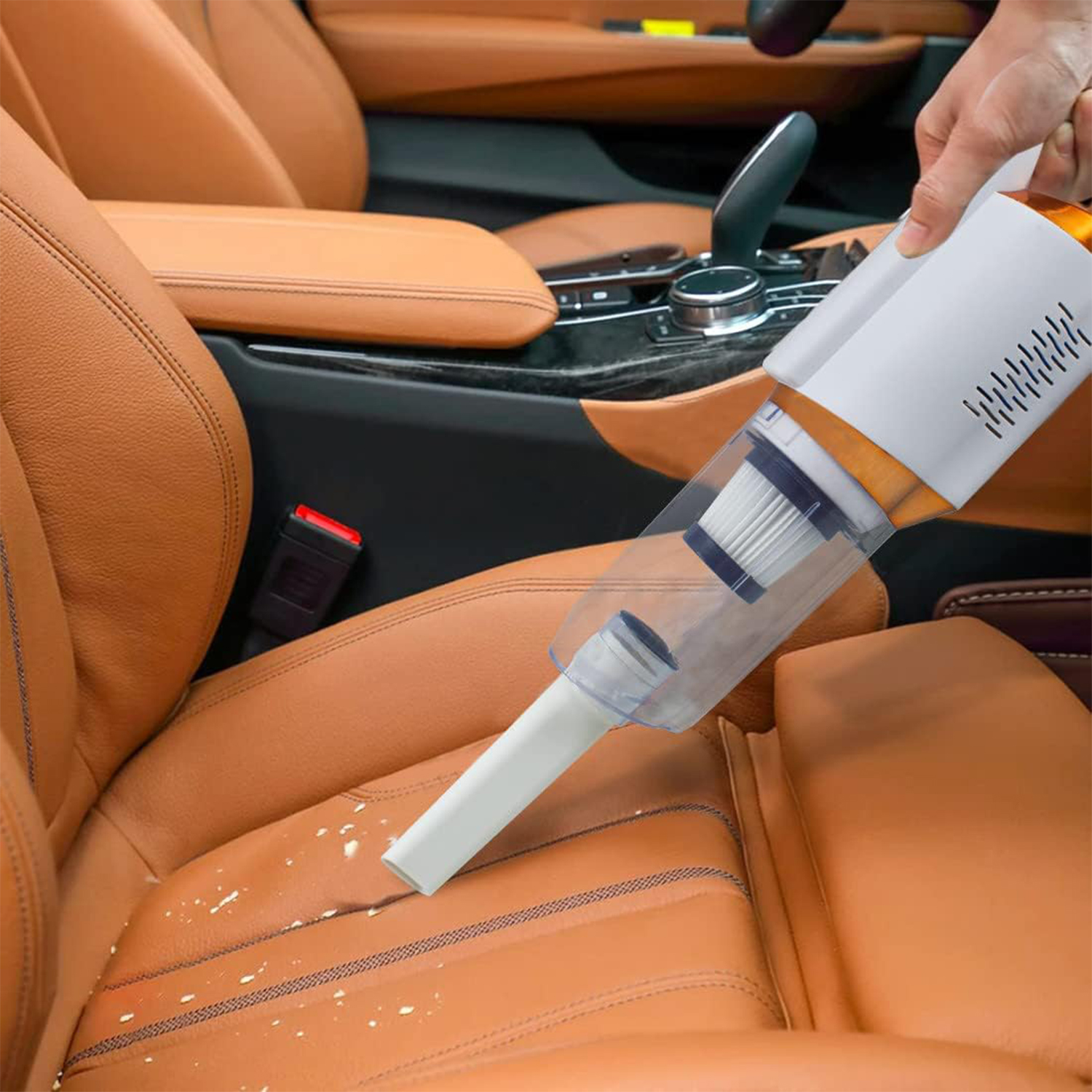 Una aspiradora de mano aspira un asiento de coche. El asiento es de cuero naranja. La aspiradora es blanca y naranja. Se ven migas en el asiento.