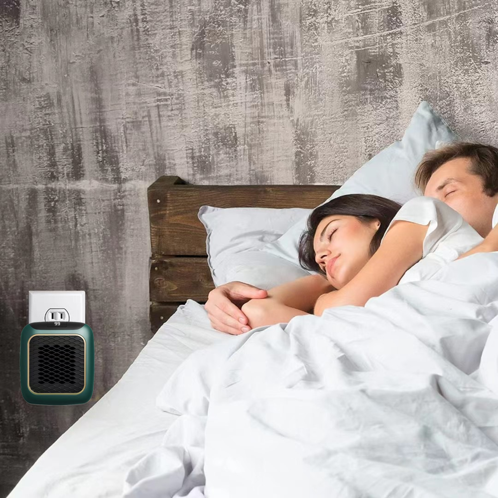 Ein Paar schläft in einem Bett. Ein kleiner grüner Heizlüfter ist in der Wand eingesteckt. Die Wand ist grau, die Bettwäsche weiß.