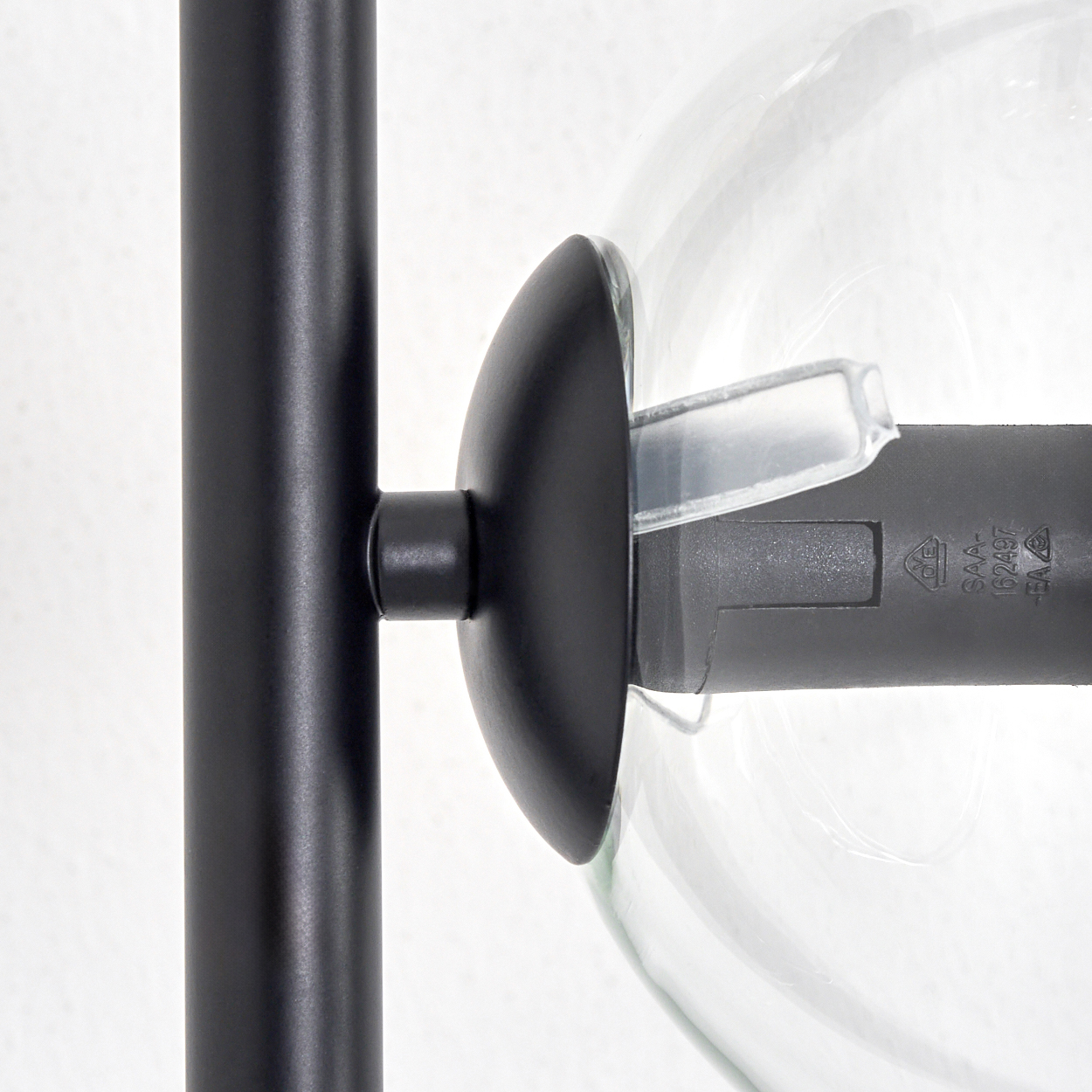 Nahaufnahme einer schwarzen Metallstruktur, die mit einer klaren Glaskugel verbunden ist. Ein weißer Hintergrund. Ein Kunststoffteil ist am Glas befestigt.