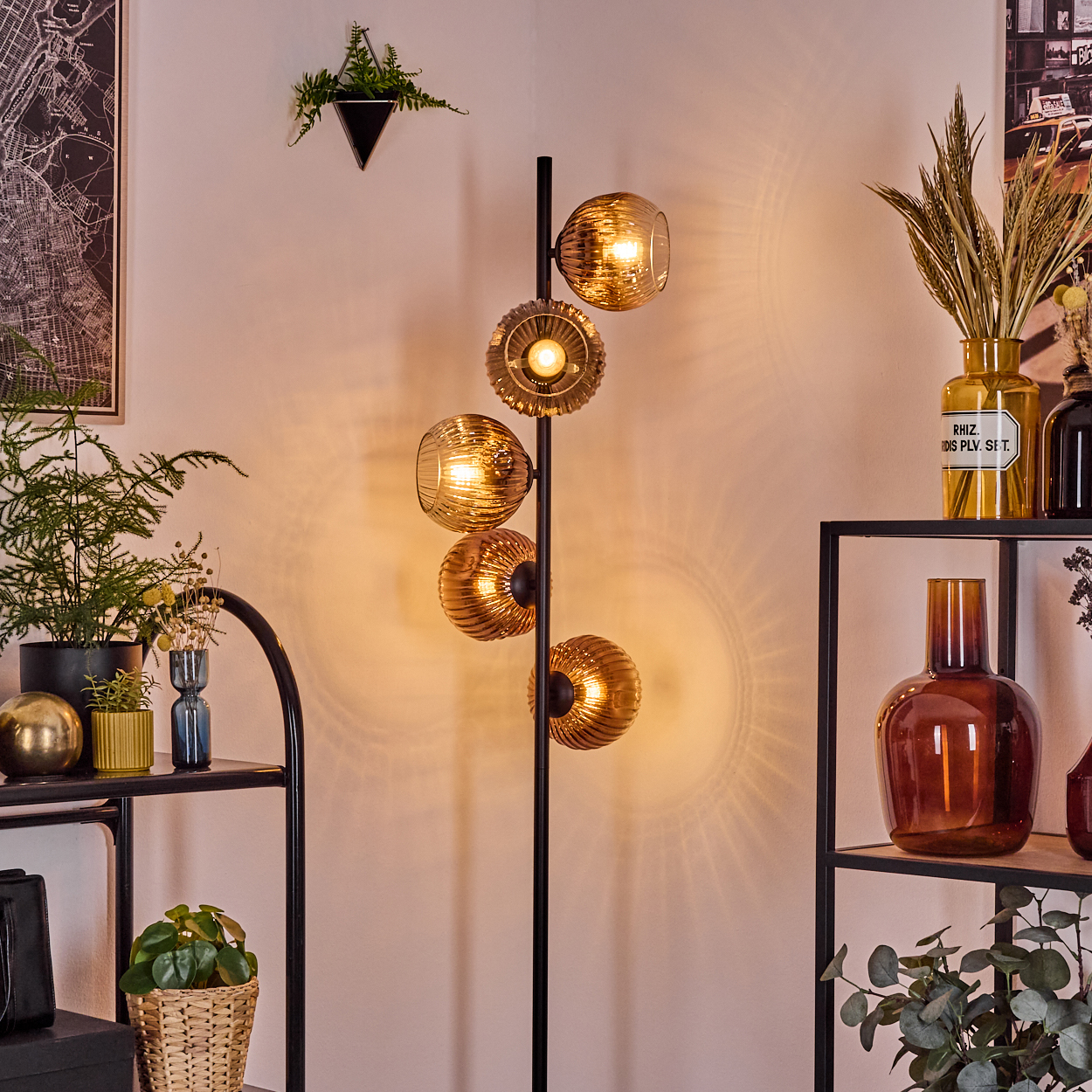 Ein modernes Zimmer mit einer Stehlampe mit bernsteinfarbenen Glaskugeln, Regalen mit Vasen, Pflanzen und einem Kartenbild.