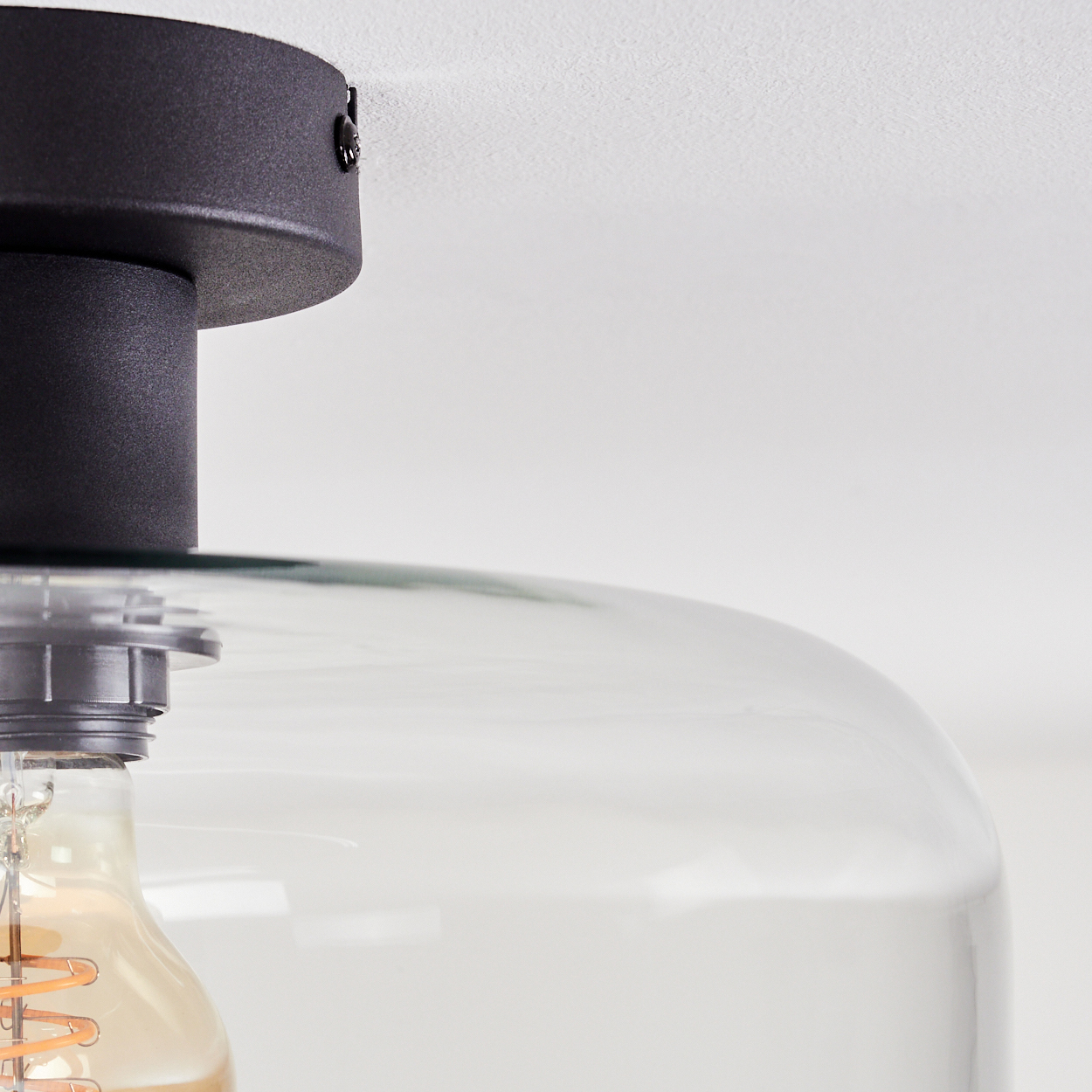 Nahaufnahme einer schwarzen Deckenlampe. Sie hat einen Glasschirm und eine sichtbare Glühbirne. Der Hintergrund ist weiß.