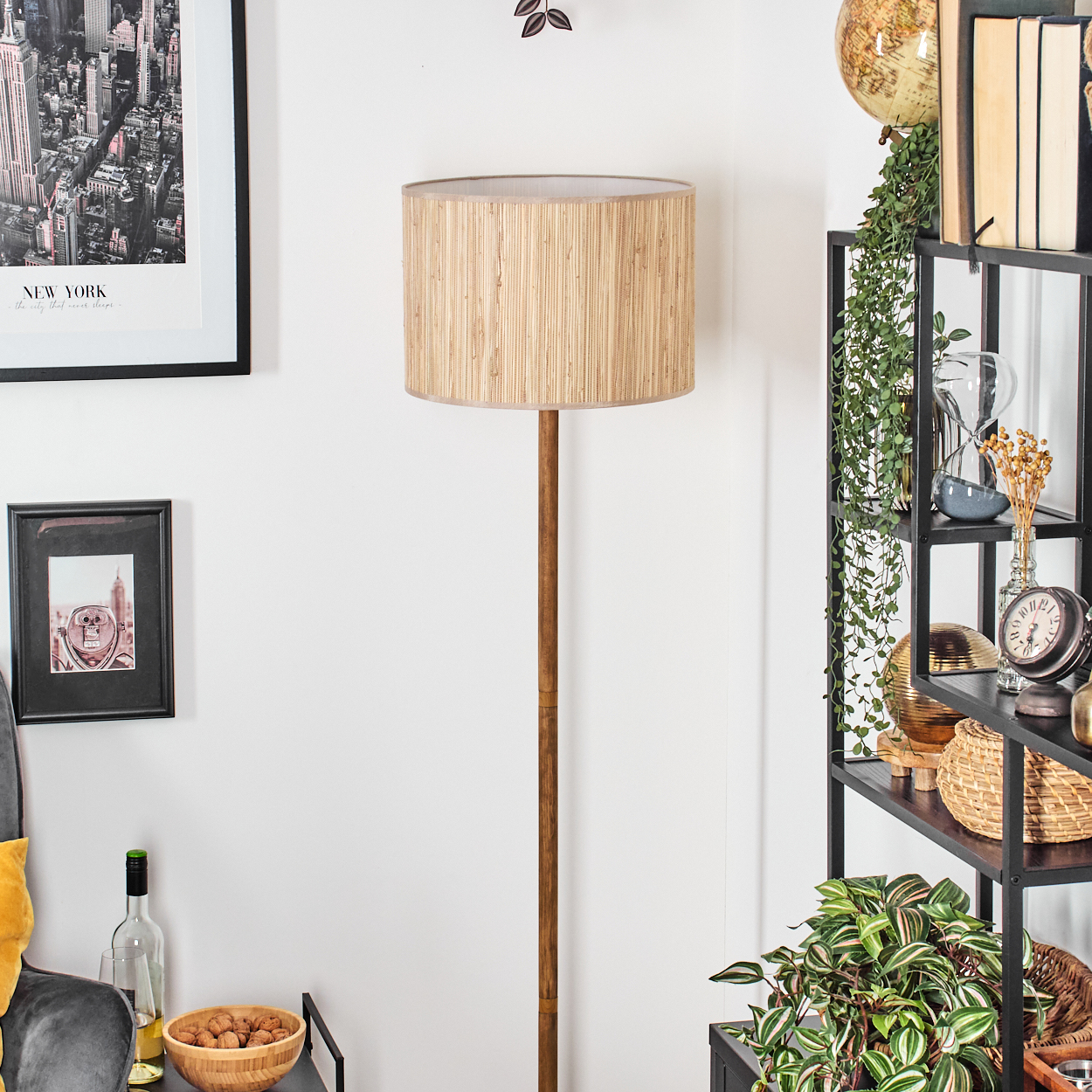 Ein Raum mit einer Holzlampe, einem New York-Bild, einem Regal mit Pflanzen, Uhr und Globus. Ein Tisch mit Walnüssen, Wein und einem Stuhl.