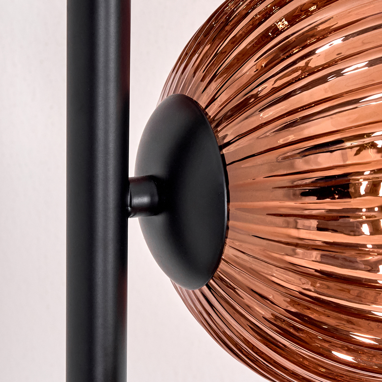 Nahaufnahme einer Lampe. Mit einem schwarzen Pfosten, einem schwarzen Kreiselement und einem kupferfarbenen, strukturierten Glasschirm.