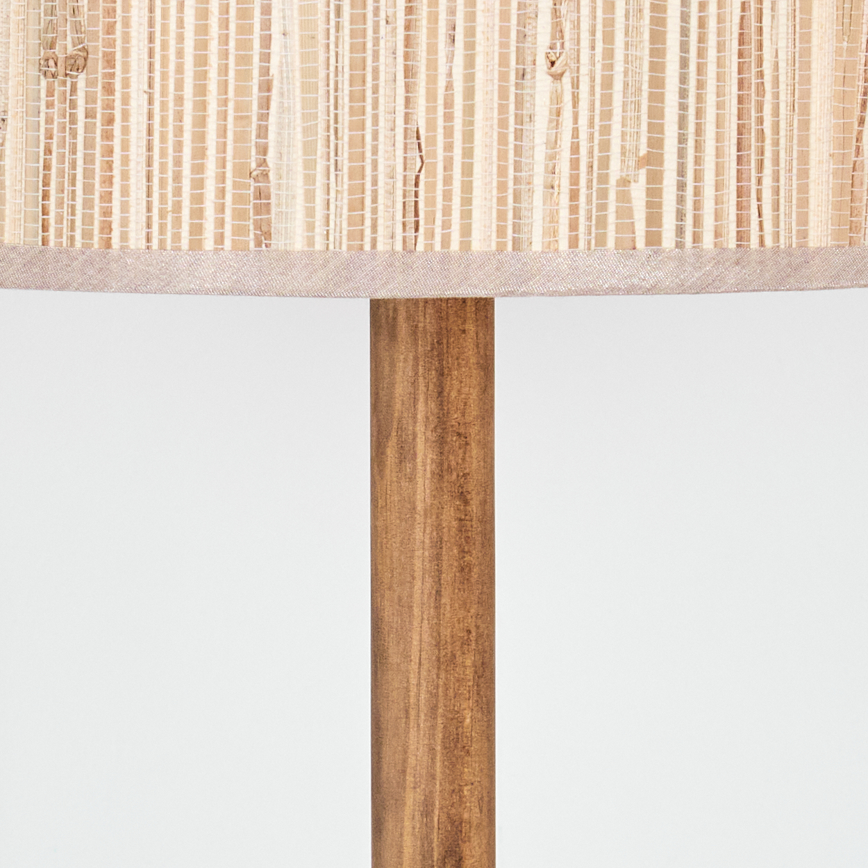 Nahaufnahme einer Lampe. Beiger gewebter Schirm sitzt auf einem Holzpfahl. Der Hintergrund ist schlicht weiß.