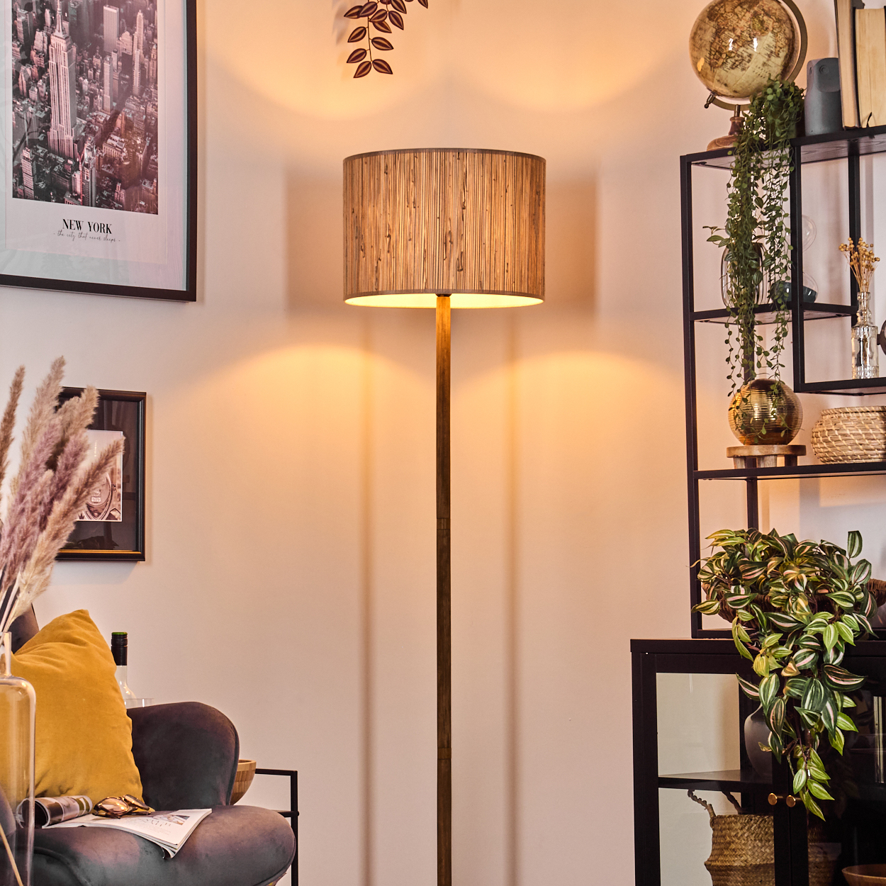 Eine Stehlampe steht in einem Raum mit schwarzem Regal, Globus und Kunst. Ein Samtstuhl mit gelbem Kissen und Pampasgras.