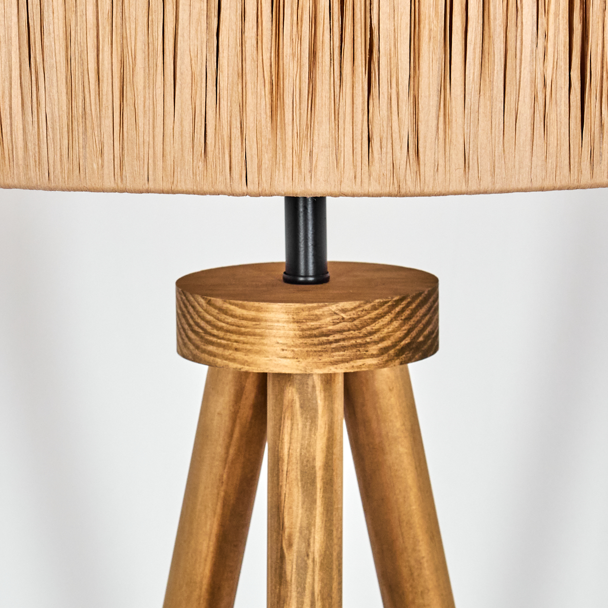 Nahaufnahme einer Lampe. Sie hat einen beigen Schirm, eine schwarze Stange und einen Holzfuß mit drei Beinen. Der Hintergrund ist weiß.