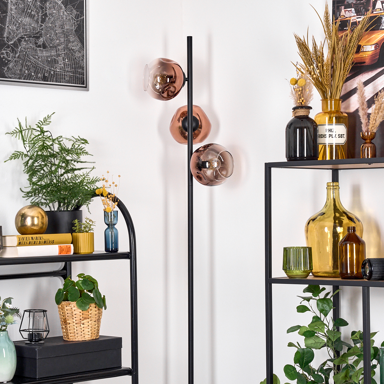 Ein Raum mit Regalen, Pflanzen und einer schwarzen Lampe mit drei kupferfarbenen Glasschirmen. Es gibt eine Karte und verschiedene Dekorationen.