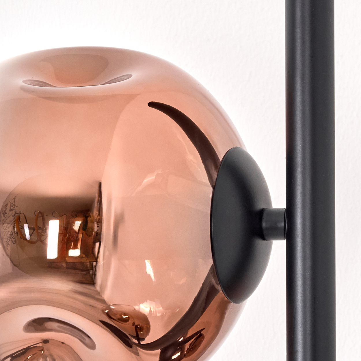 Nahaufnahme einer modernen Lampe. Sie hat einen kugelförmigen, kupferfarbenen Glasschirm, eine schwarze Metallhalterung und eine sichtbare Glühbirne.