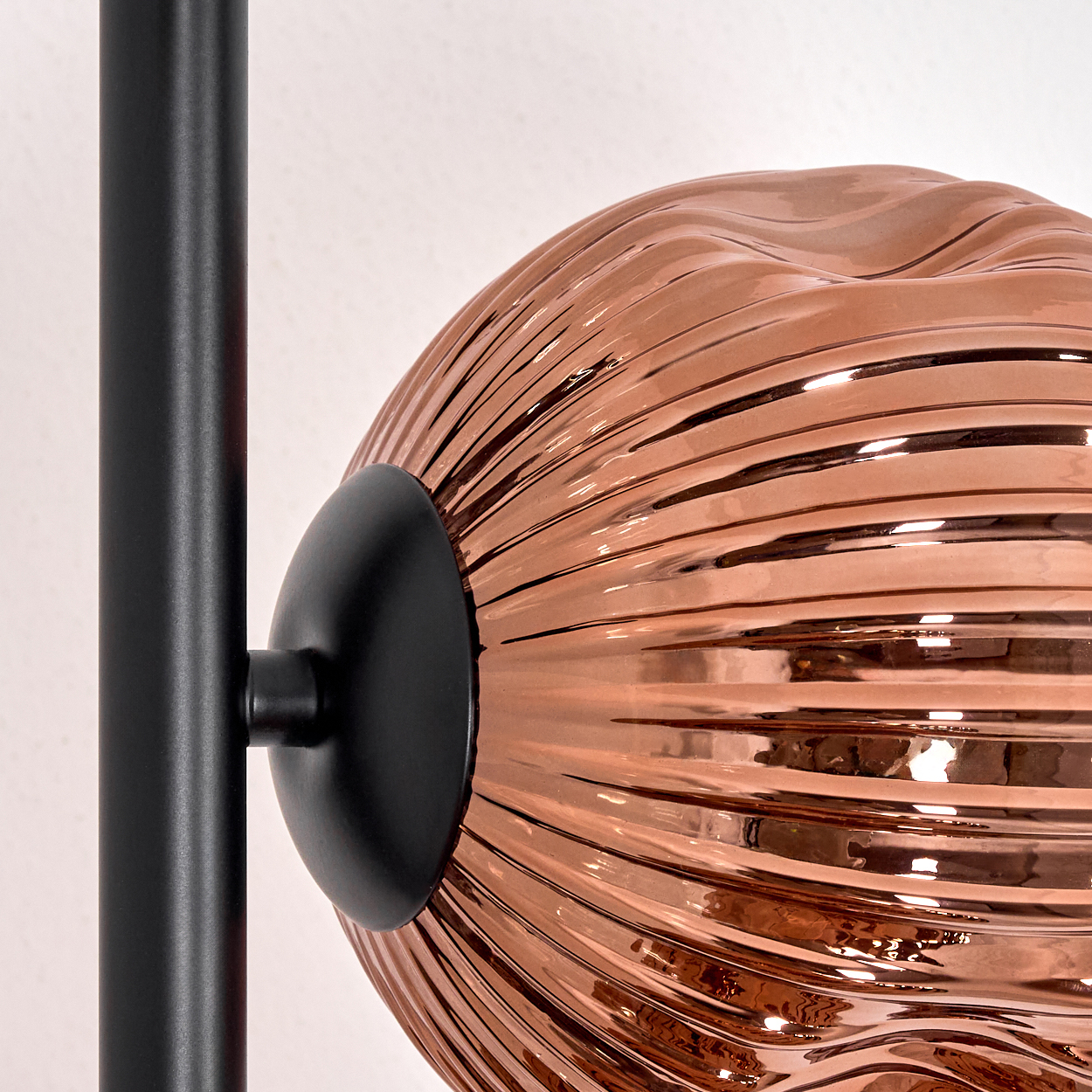 Nahaufnahme einer Lampe. Sie hat eine kupferfarbene, strukturierte Kugel, die an einer schwarzen Metallstange befestigt ist.