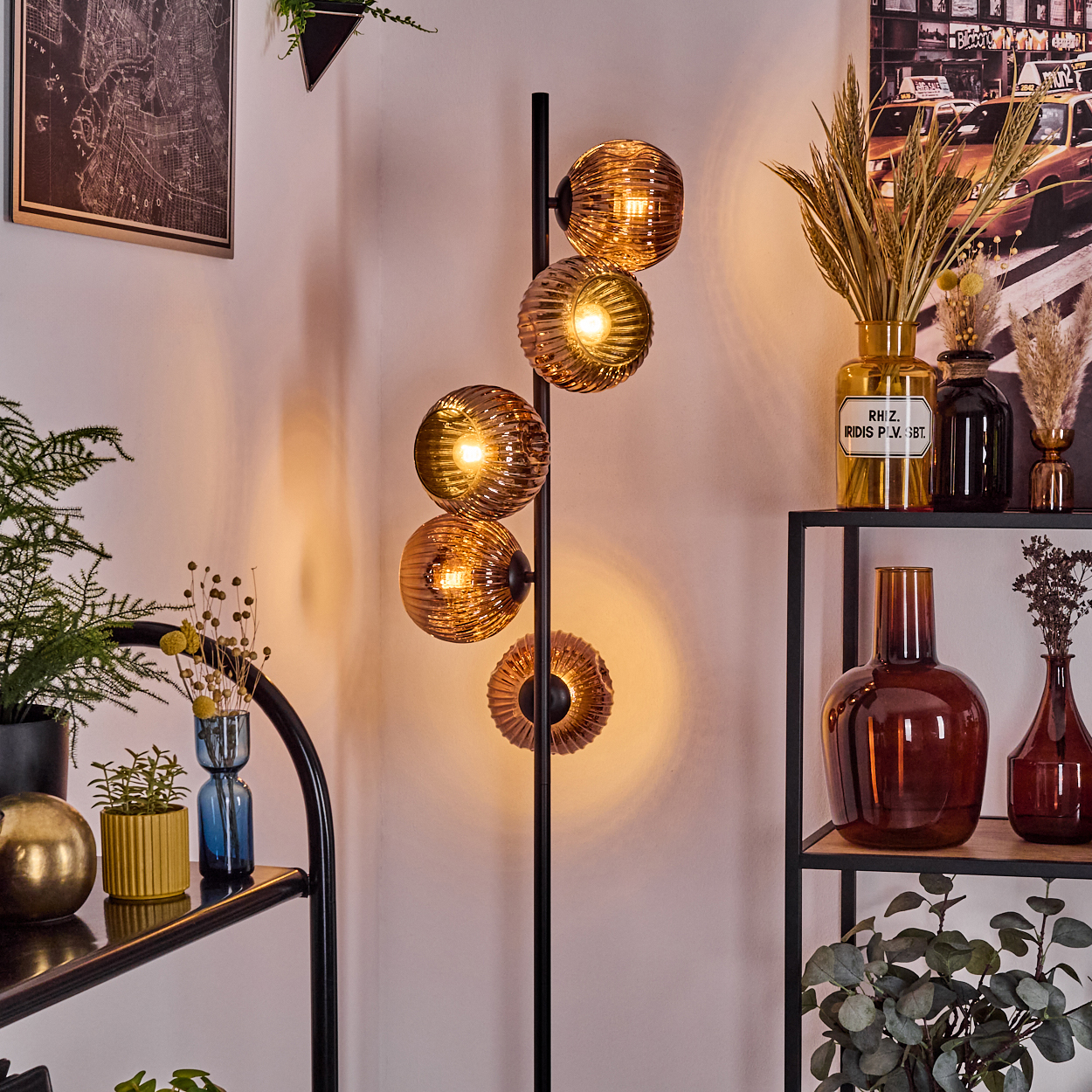 Eine Stehlampe mit bernsteinfarbenen Glaskugeln leuchtet. Regale halten Vasen, Pflanzen und ein Foto von New York City.