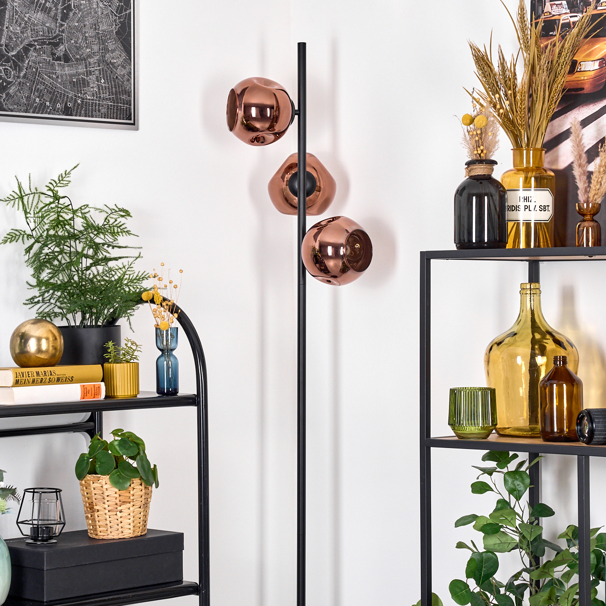 Ein modernes Interieur mit schwarzem Regal, Pflanzen, einer Stehlampe mit Kupferschirmen und dekorativen Gegenständen. Die Wand ist weiß.