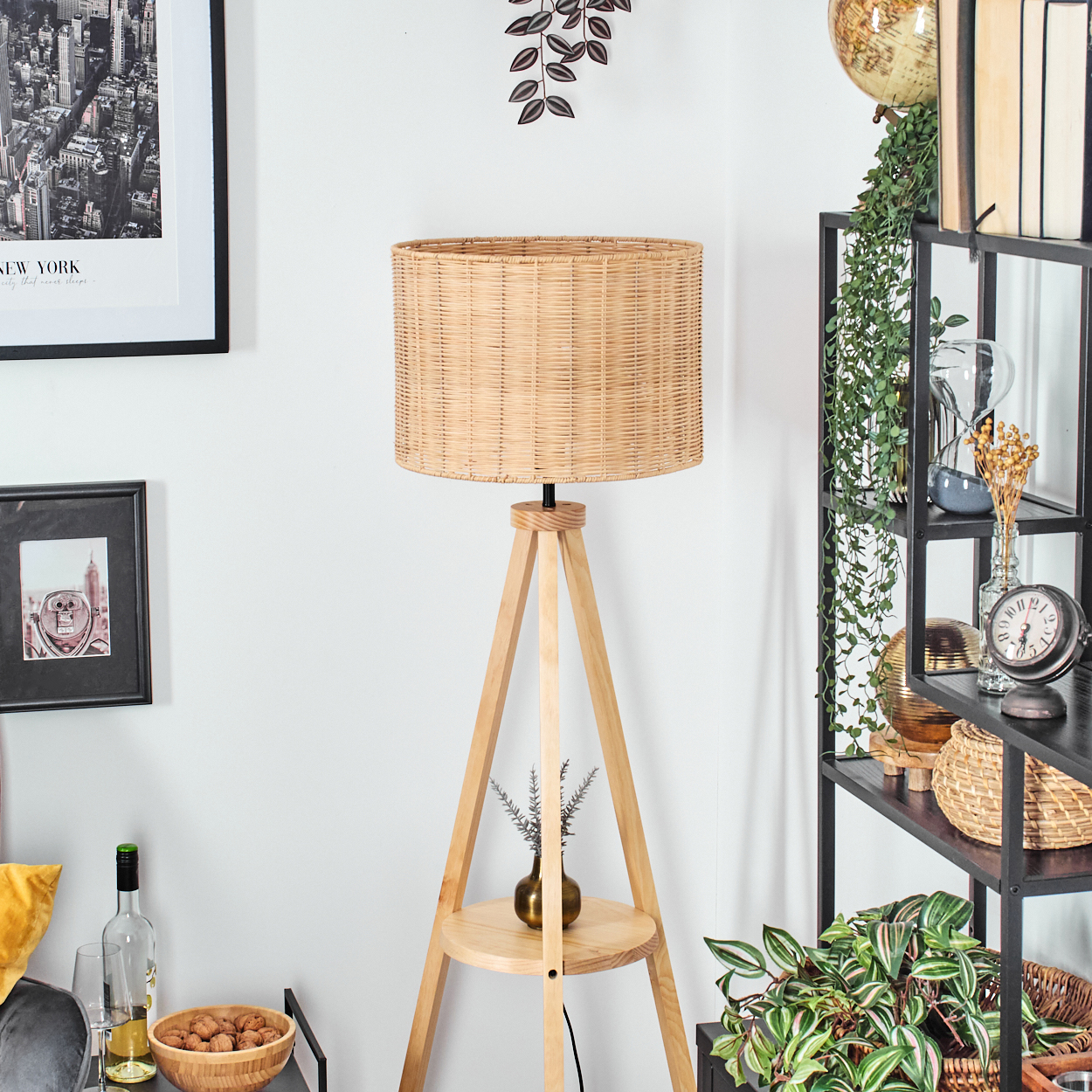 Ein Raum mit einer Holzlampe, einem schwarzen Regal mit Dekorationen und einem New York-Bild. Die Lampe hat einen gewebten Schirm.
