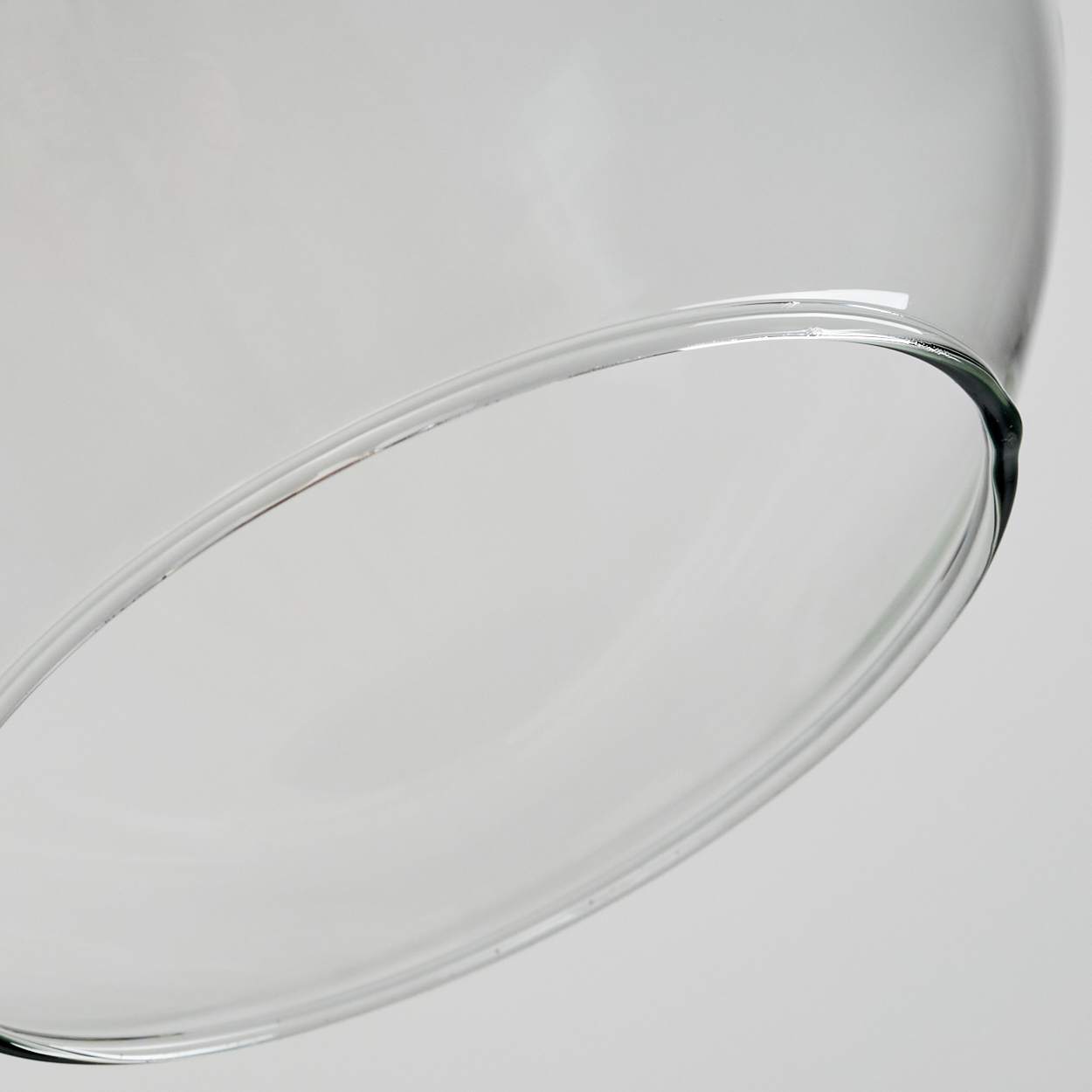 Nahaufnahme eines transparenten Glasobjekts. Der gebogene Rand ist vor einem weißen Hintergrund fokussiert.