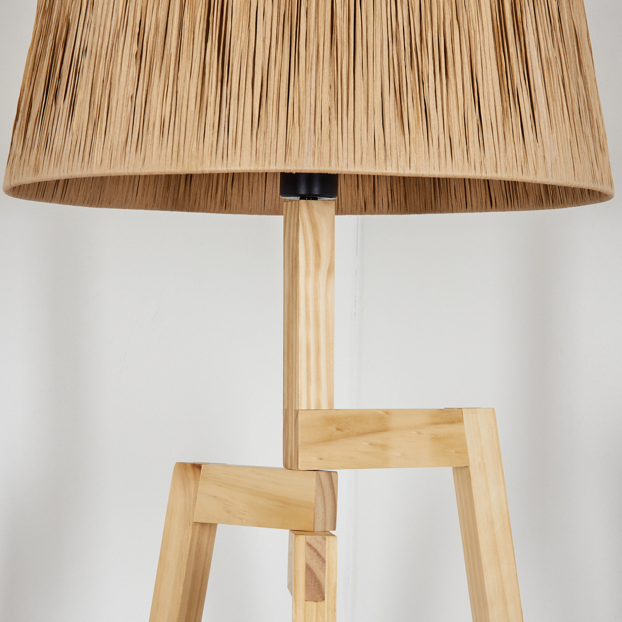 Nahaufnahme einer Lampe mit beigem Schirm und Holzfuß. Der Schirm besteht aus strukturiertem Material. Der Ständer ist aus hellem Holz gefertigt.
