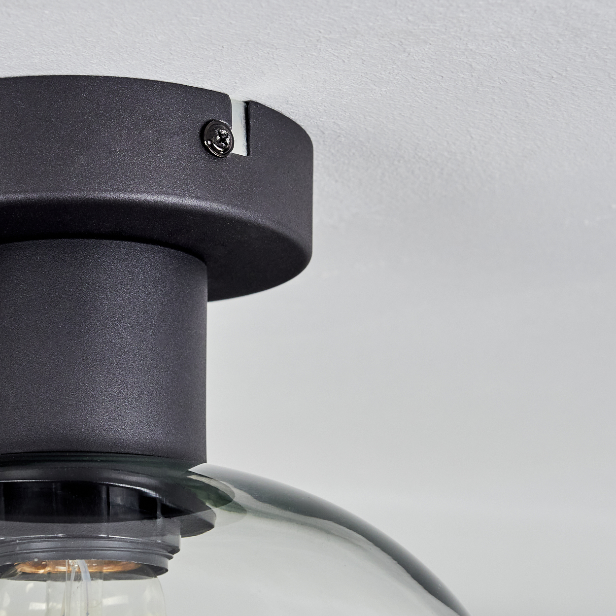 Nahaufnahme einer schwarzen Deckenlampe. Sie hat ein abgerundetes Design mit Glasschirm und sichtbarer Glühbirne. Die Lampe ist an einer weißen Decke befestigt.