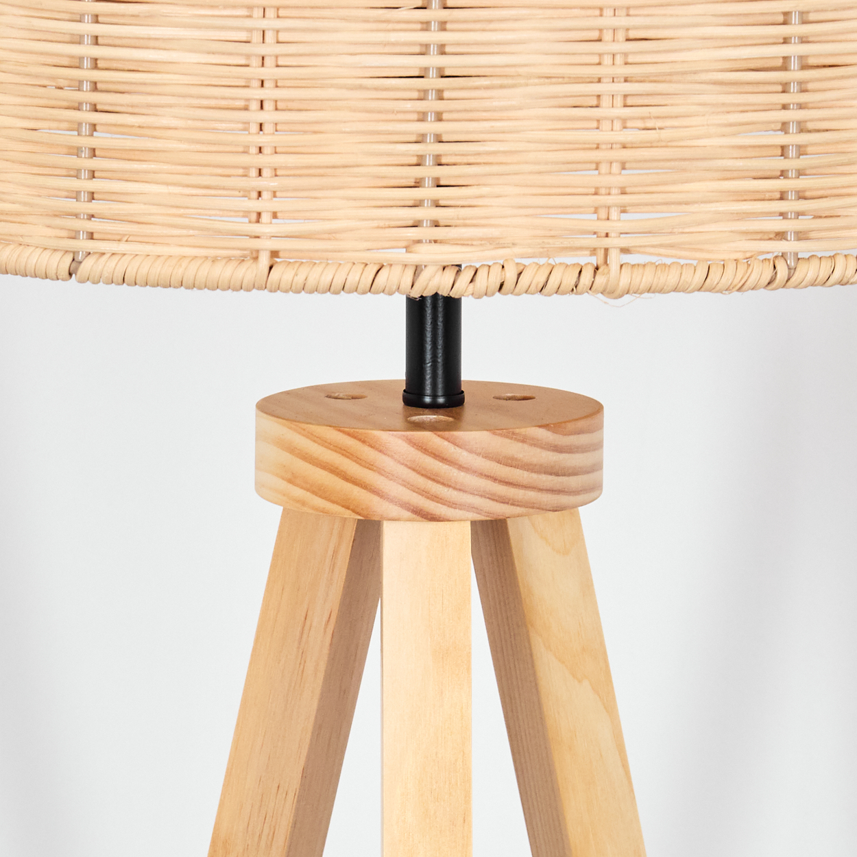 Nahaufnahme einer Lampe mit Korbschatten, schwarzem Pfosten und Holzsockel. Die Lampe steht auf drei Holzbeinen vor weißem Hintergrund.