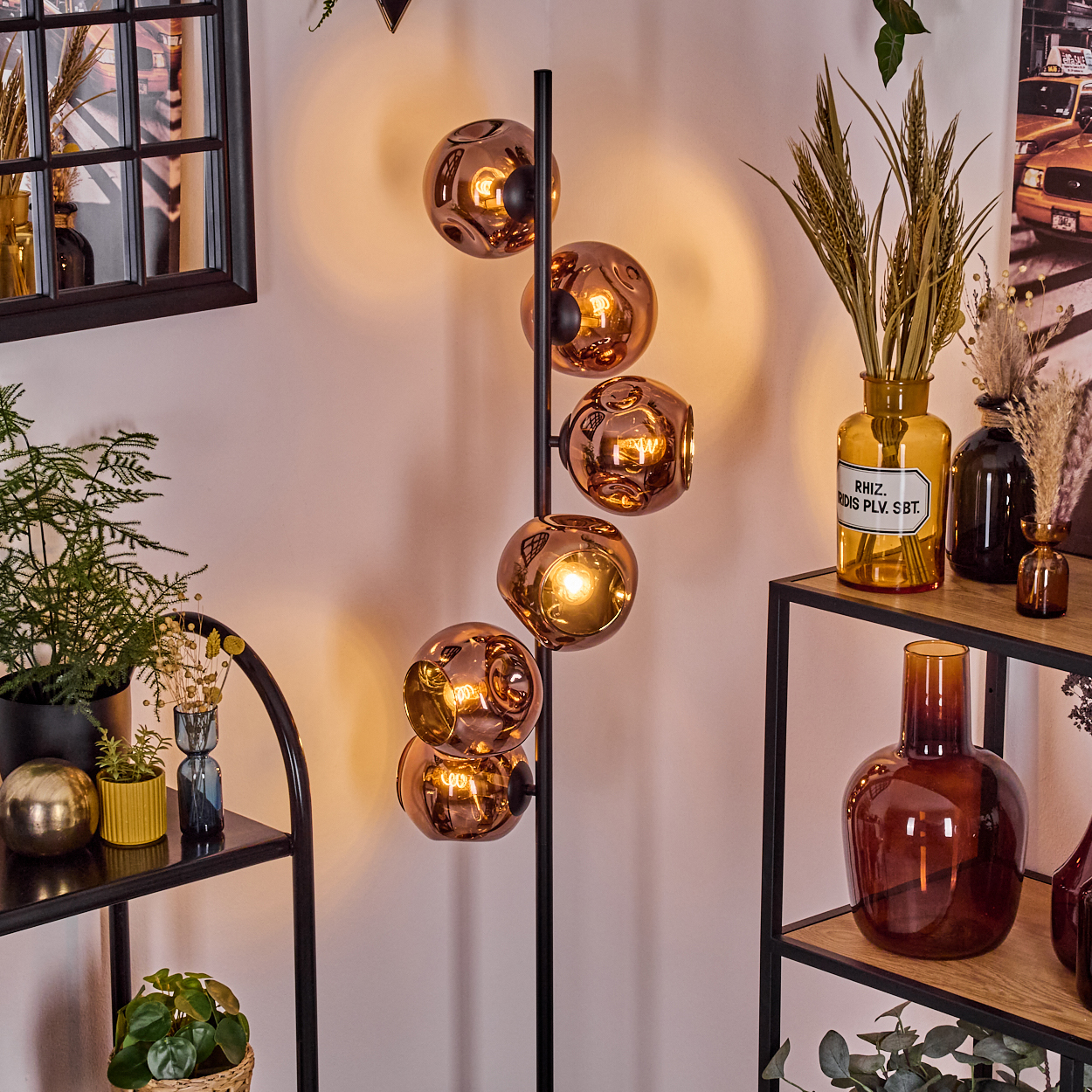 Ein modernes Zimmer mit einer Stehlampe mit Kupfersphären. Regale beherbergen Vasen, Pflanzen und Dekorationsartikel. Warme Beleuchtung schafft eine gemütliche Atmosphäre.