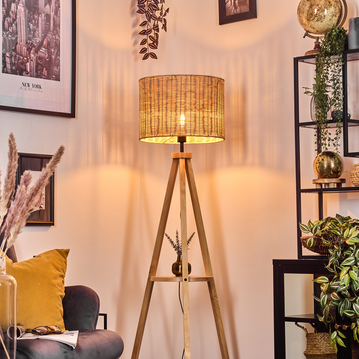 Eine beleuchtete Holz-Dreibein-Lampe mit gewebtem Schirm. Die Szene umfasst einen Stuhl, Regale mit Pflanzen und ein New York City Poster.
