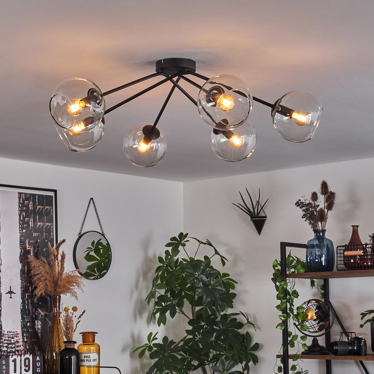 Eine moderne Deckenleuchte mit Glaskugeln beleuchtet einen Raum mit Pflanzen, einem Spiegel und Regalen mit verschiedenen Gegenständen.