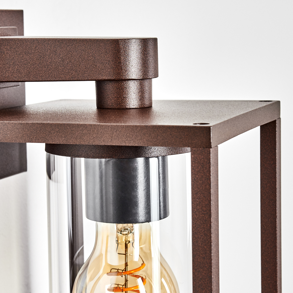 Nahaufnahme einer braunen Metalllampe. Sie hat einen Glaszylinder mit einer Glühbirne. Der Hintergrund ist weiß.