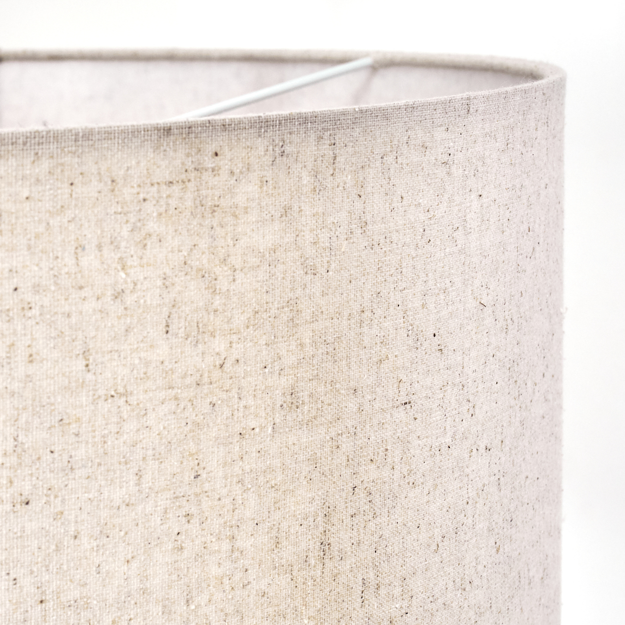 Nahaufnahme eines Lampenschirms. Es ist ein hellbeige Stoffzylinder. Ein weißes Metallgestell ist oben vor weißem Hintergrund zu sehen.
