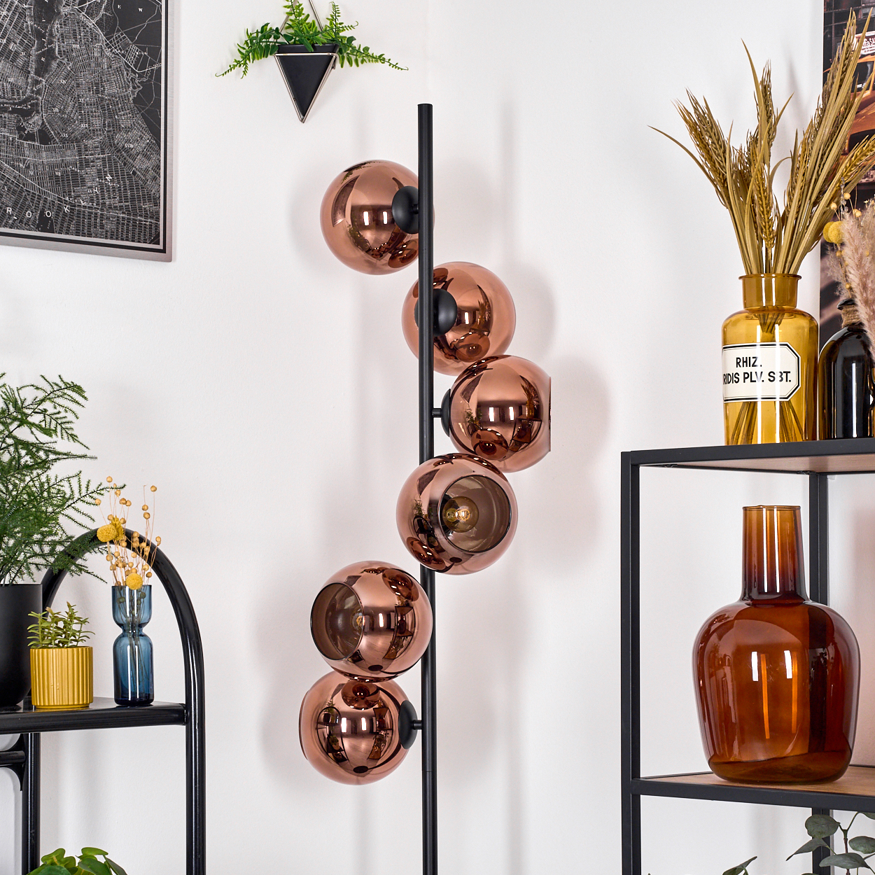 Ein modernes Interieur mit einer kupferfarbenen Kugellampe, Pflanzen und Regalen mit Vasen.