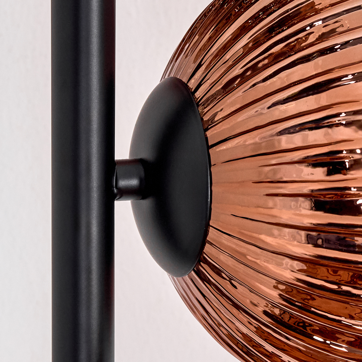 Nahaufnahme einer modernen Lampe. Sie hat einen schwarzen Pfosten, eine schwarze kreisförmige Basis und eine kupferfarbene, strukturierte Glaskugel.