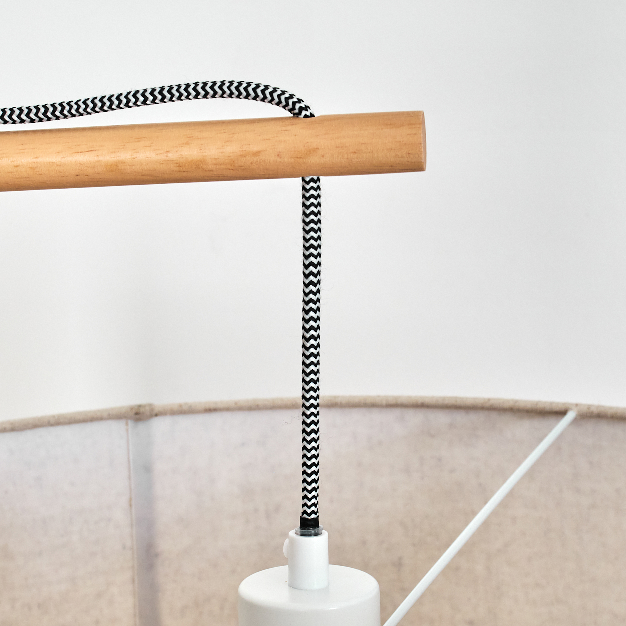 Nahaufnahme einer Lampe. Ein Holzstab hält ein schwarz-weiß gestreiftes Kabel. Unterhalb befinden sich ein weißer Lampensockel und ein beiger Lampenschirm.