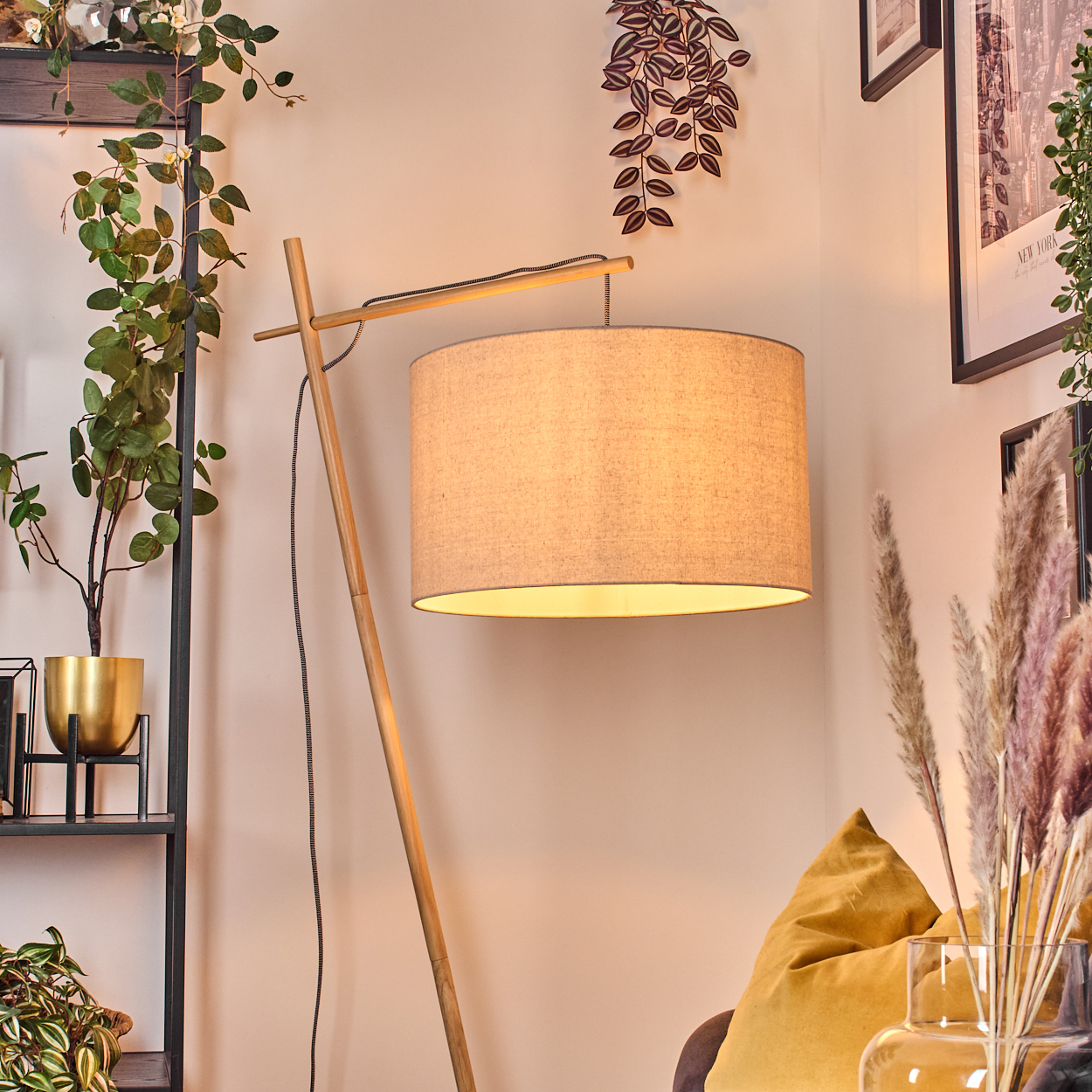 Ein modernes Wohnzimmer mit einer hölzernen Stehlampe mit beigem Lampenschirm, Pflanzen und einem gelben Kissen.