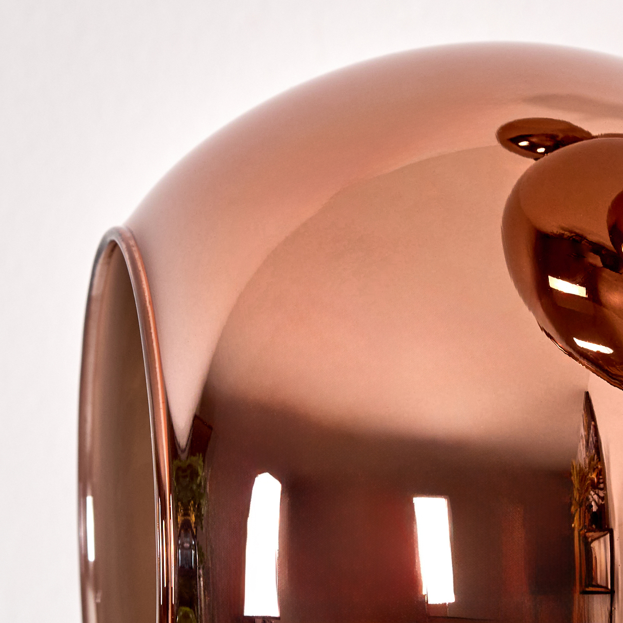 Nahaufnahme eines kupferfarbenen, reflektierenden Objekts, möglicherweise einer Lampe. Die Oberfläche reflektiert Licht und die Umgebung.