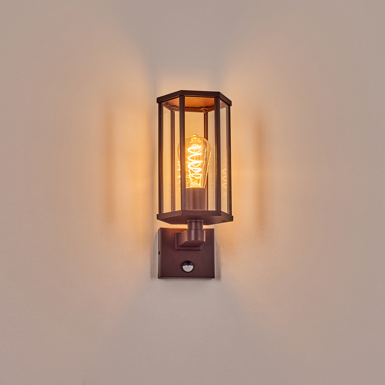 Dunkle Metall-Außenwandleuchte mit Glühbirne. Die Lampe ist an einer hellbeige Wand montiert.
