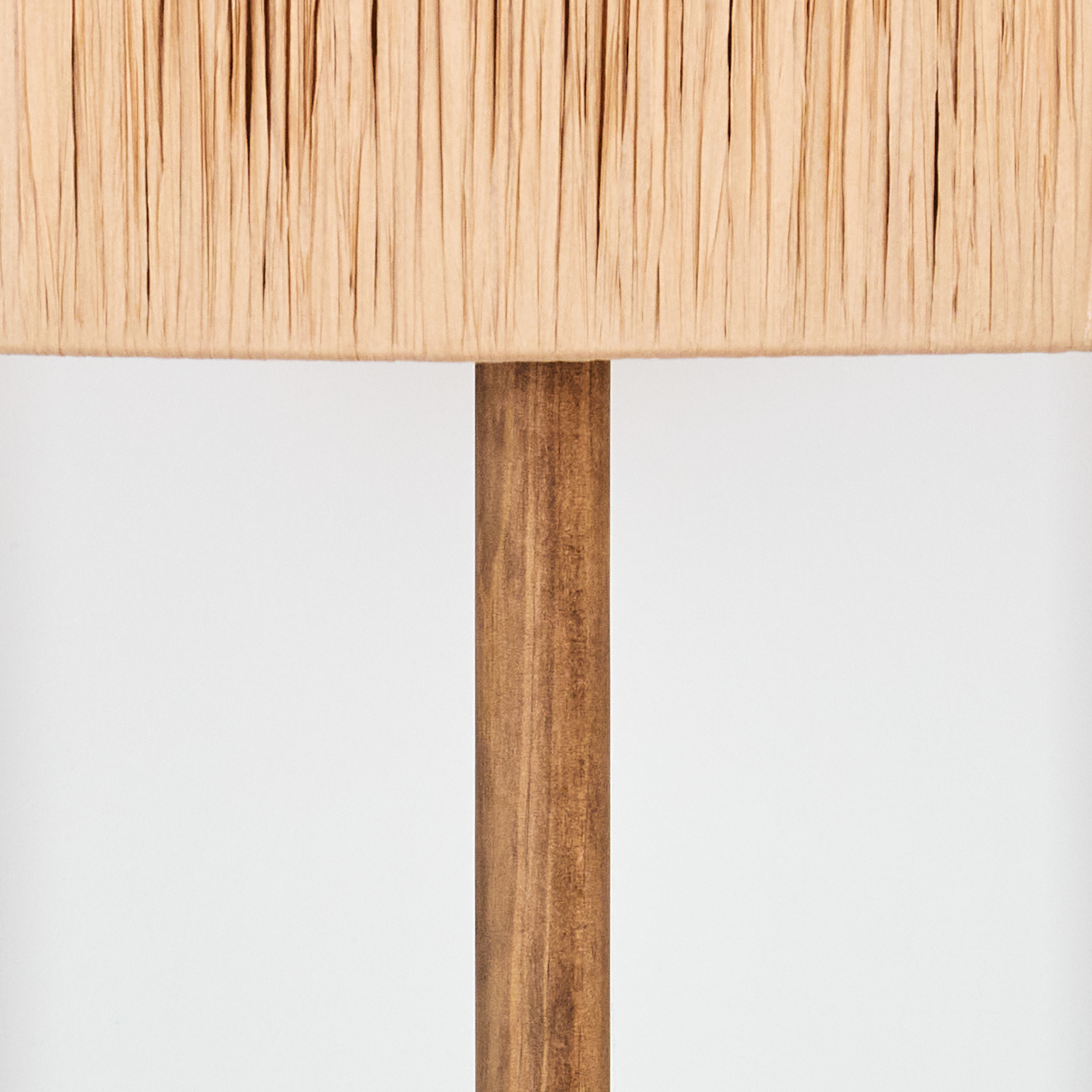 Nahaufnahme einer Lampe. Der Lampenschirm ist aus beigem, plissiertem Stoff. Der Pfosten ist aus braunem Holz. Der Hintergrund ist weiß.