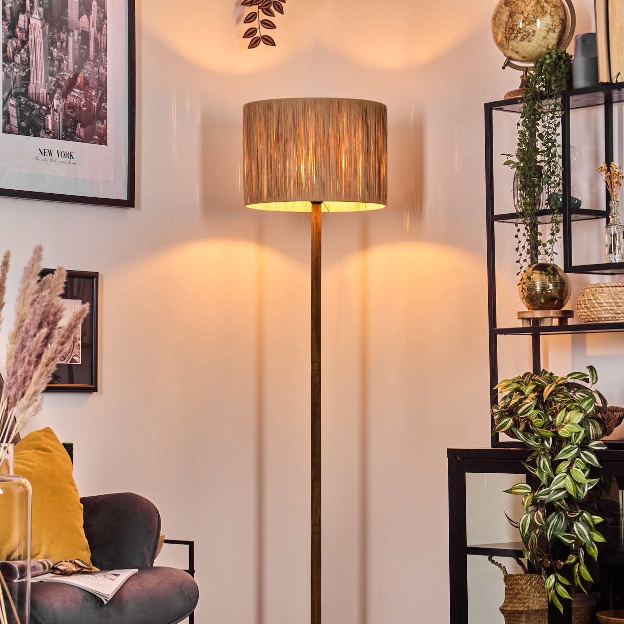 Eine Stehlampe steht in einem Raum mit Regal, Pflanzen und einem New York City Poster. Ein Stuhl und eine Vase sind ebenfalls sichtbar.