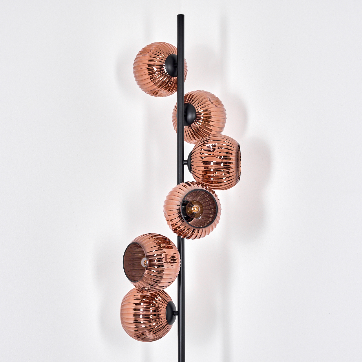 Eine moderne Stehlampe mit kupferfarbenen Glasschirmen, vertikal angeordnet, vor weißer Wand.