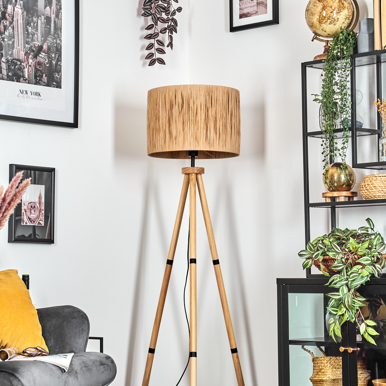 Ein Raum mit einer hölzernen Stativlampe. Ein schwarzes Metallregal mit Pflanzen und einem Globus. Ein grauer Sessel mit gelbem Kissen.
