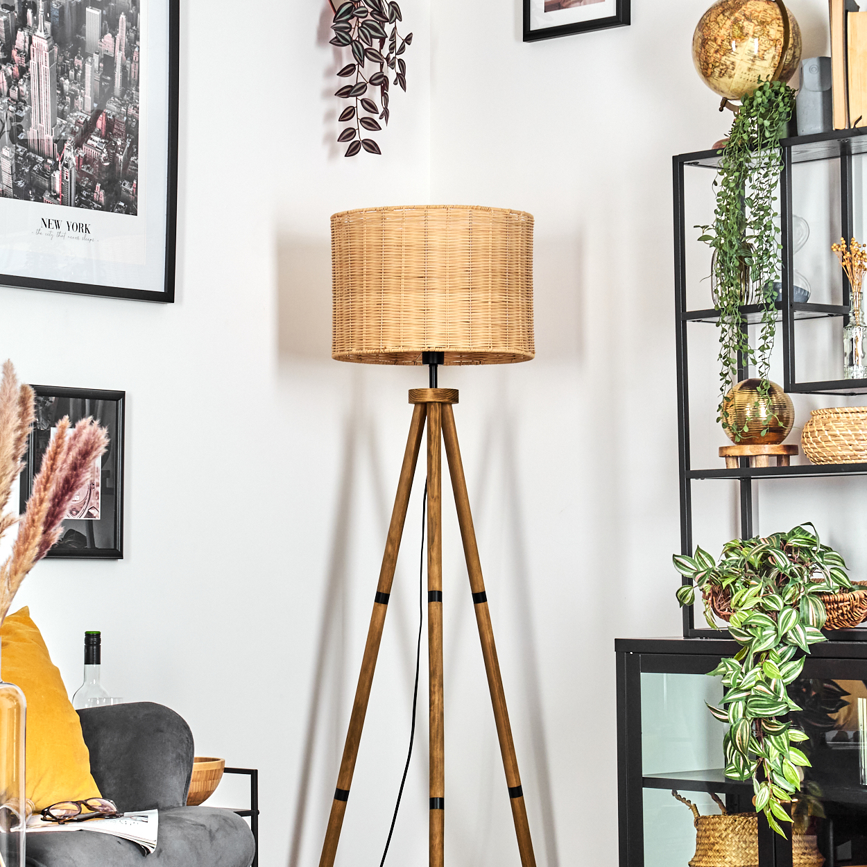 Ein Raum mit einer hölzernen Stativlampe, einem schwarzen Regal und einem gerahmten New York-Bild. Pflanzen und Dekoration sind ebenfalls vorhanden.