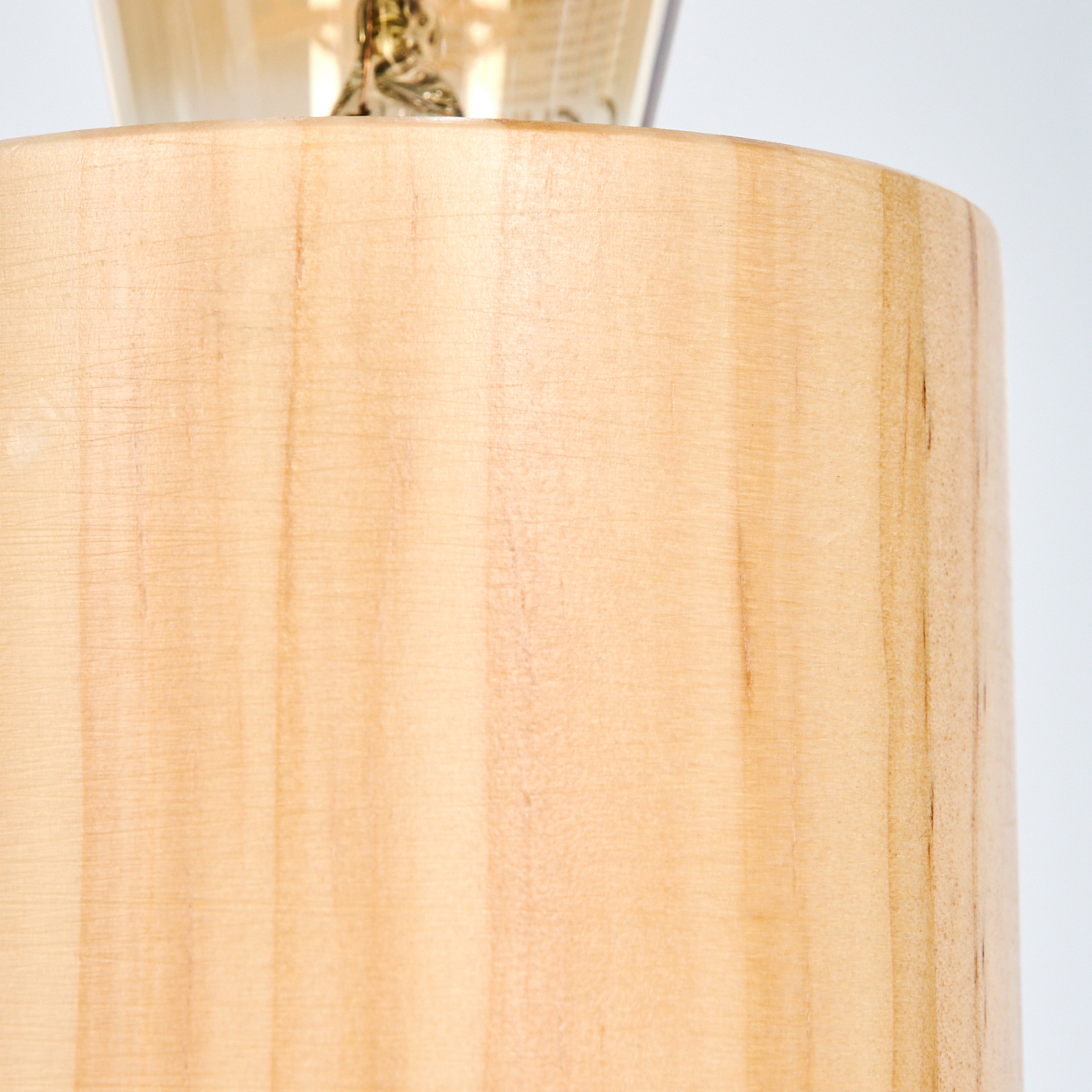 Nahaufnahme einer Holzlampe. Der Lampenschirm ist zylindrisch, aus hellem Holz mit Maserung. Der Hintergrund ist weiß.