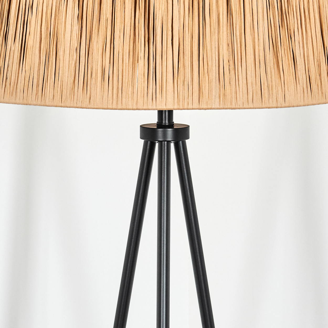 Nahaufnahme einer Stehlampe. Der Lampenschirm ist beige, das Gestell schwarz und hat ein Stativdesign. Der Hintergrund ist weiß.