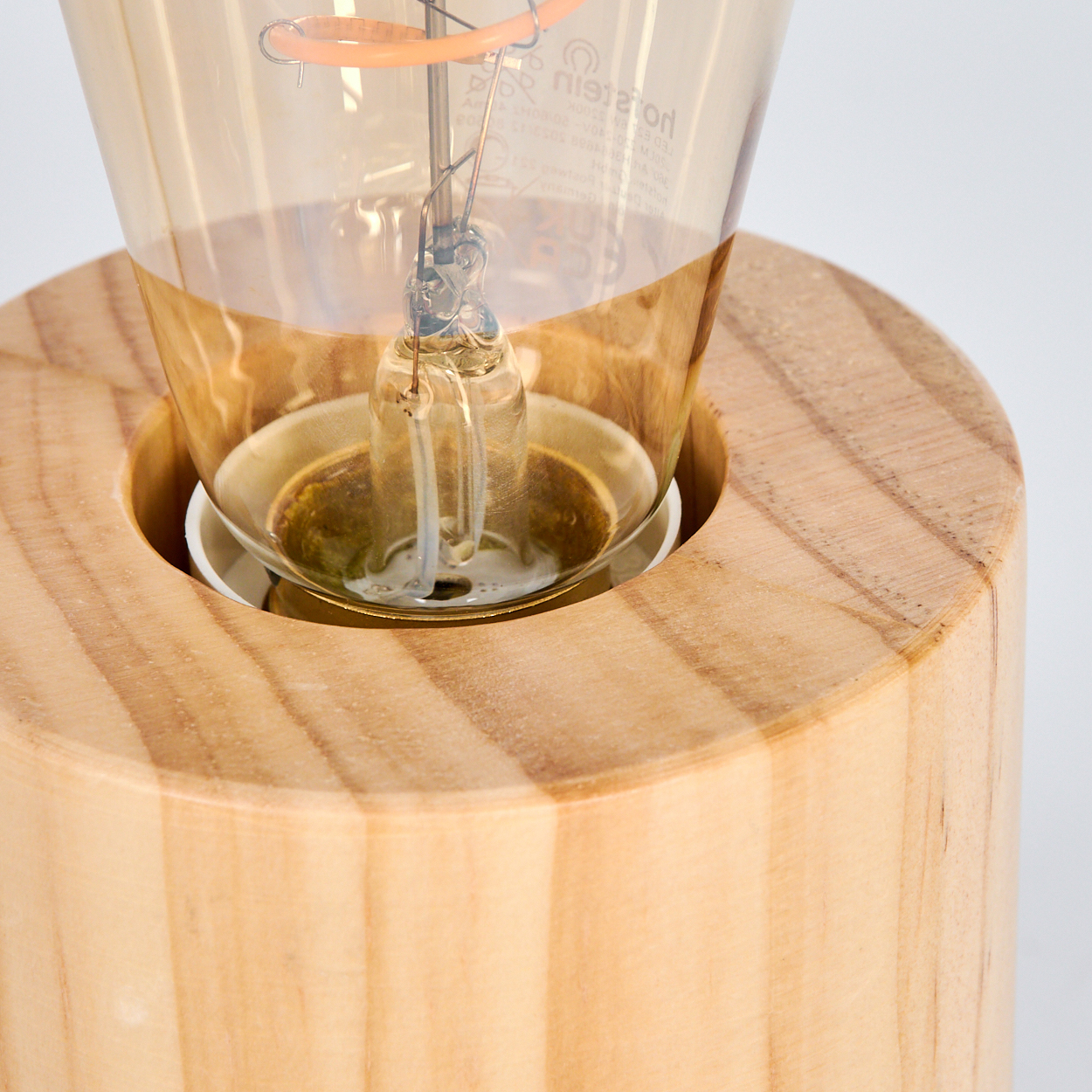 Nahaufnahme einer Glühbirne in einem Holzsockel. Die Birne ist aus Glas und hat einen warmen Schein, vor weißem Hintergrund.