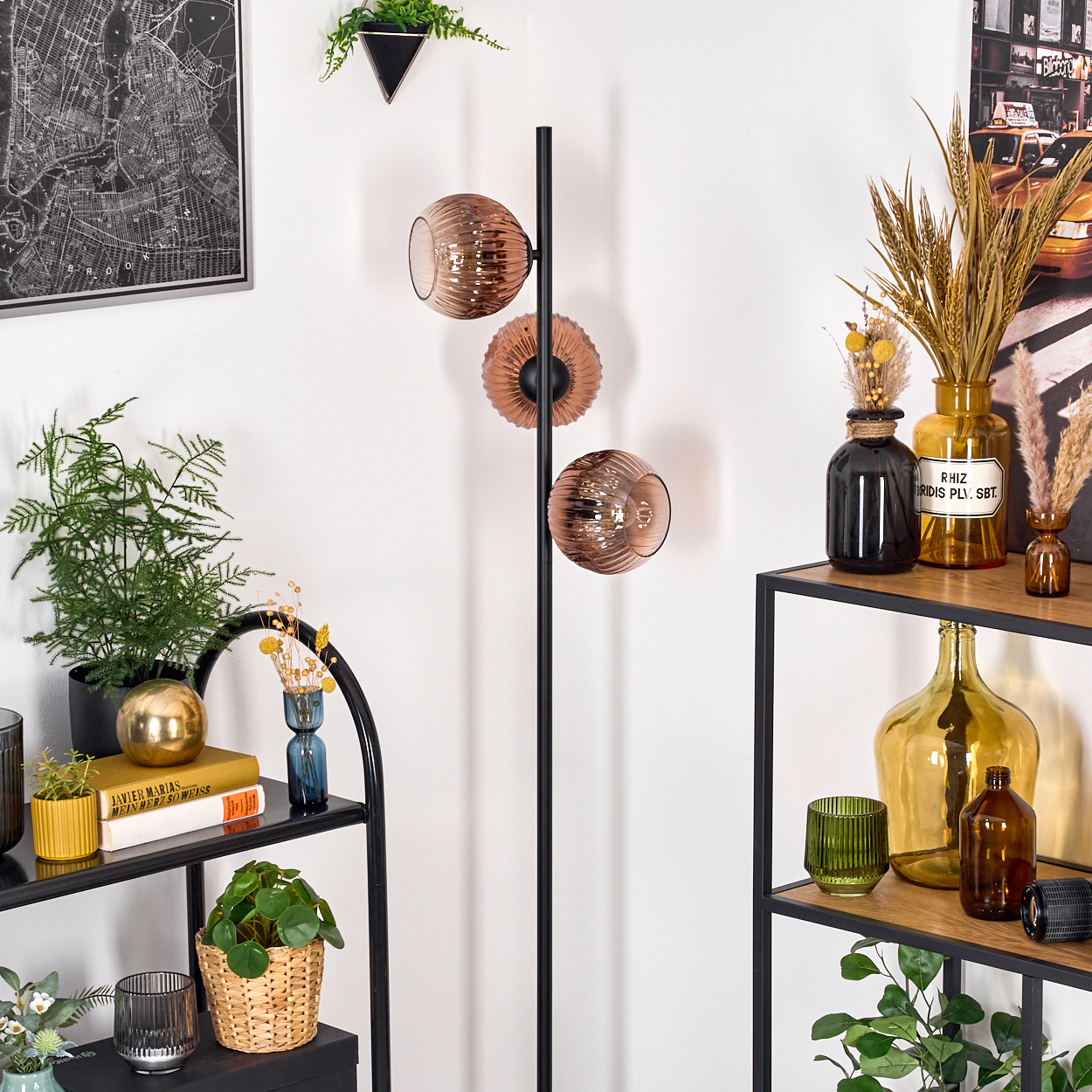 Ein modernes Interieur mit schwarzer Lampe, Regalen mit Pflanzen und Dekoration. Eine Karte und ein New York-Poster sind sichtbar.