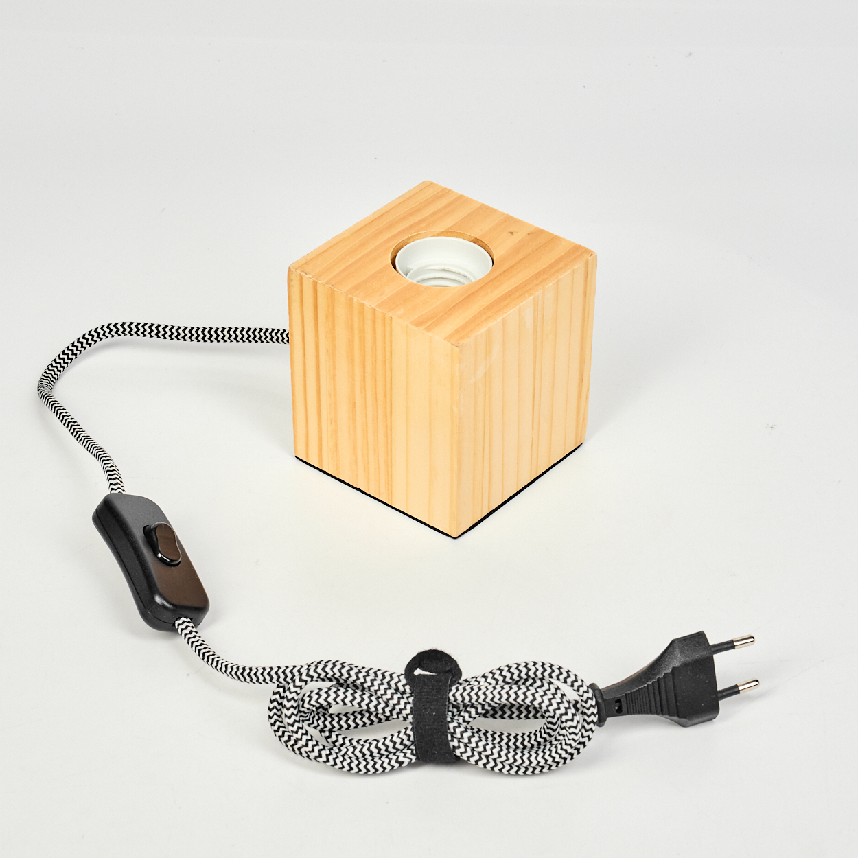 Eine Holzquaderlampe mit einem schwarz-weißen Zickzack-Kabel, Schalter und Stecker auf weißem Hintergrund.