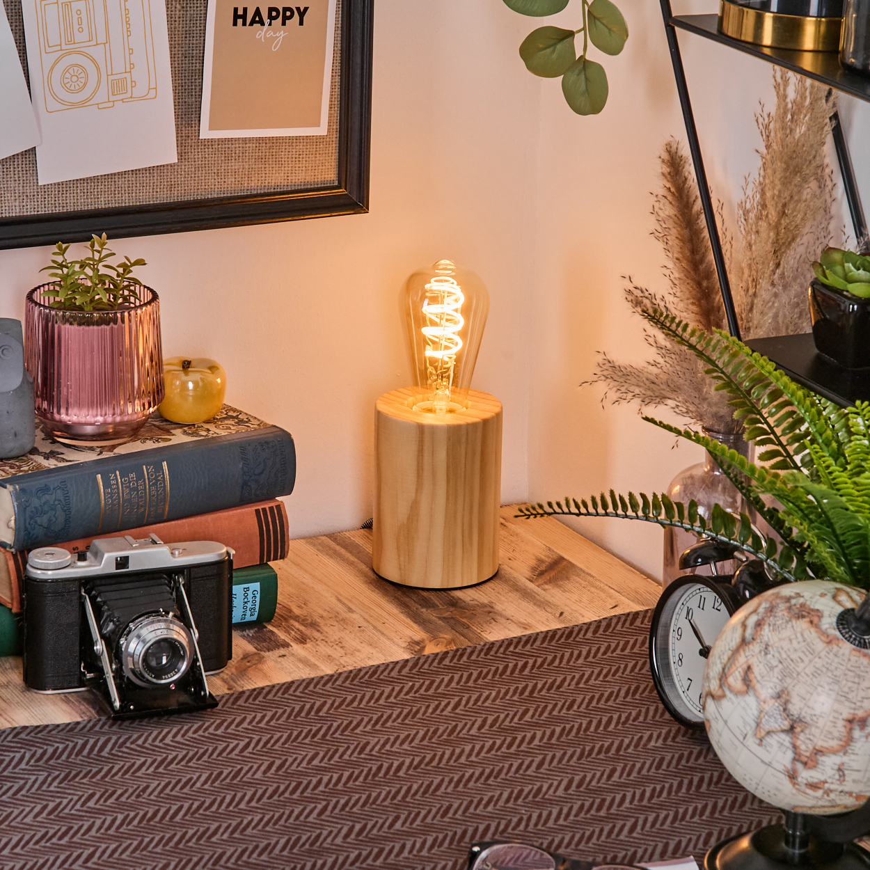 Ein Schreibtisch mit Lampe, Büchern, Kamera, Globus, Uhr und Pflanzen. Ein Zettel mit 'Happy day' an der Wand.