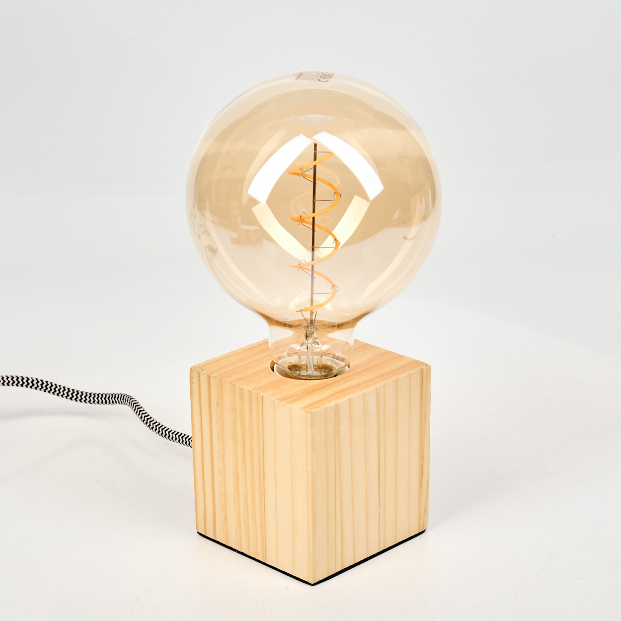 Eine dekorative Lampe mit einer großen, runden, bernsteinfarbenen Glühbirne auf einem Holzsockel mit schwarz-weißem Kabel.