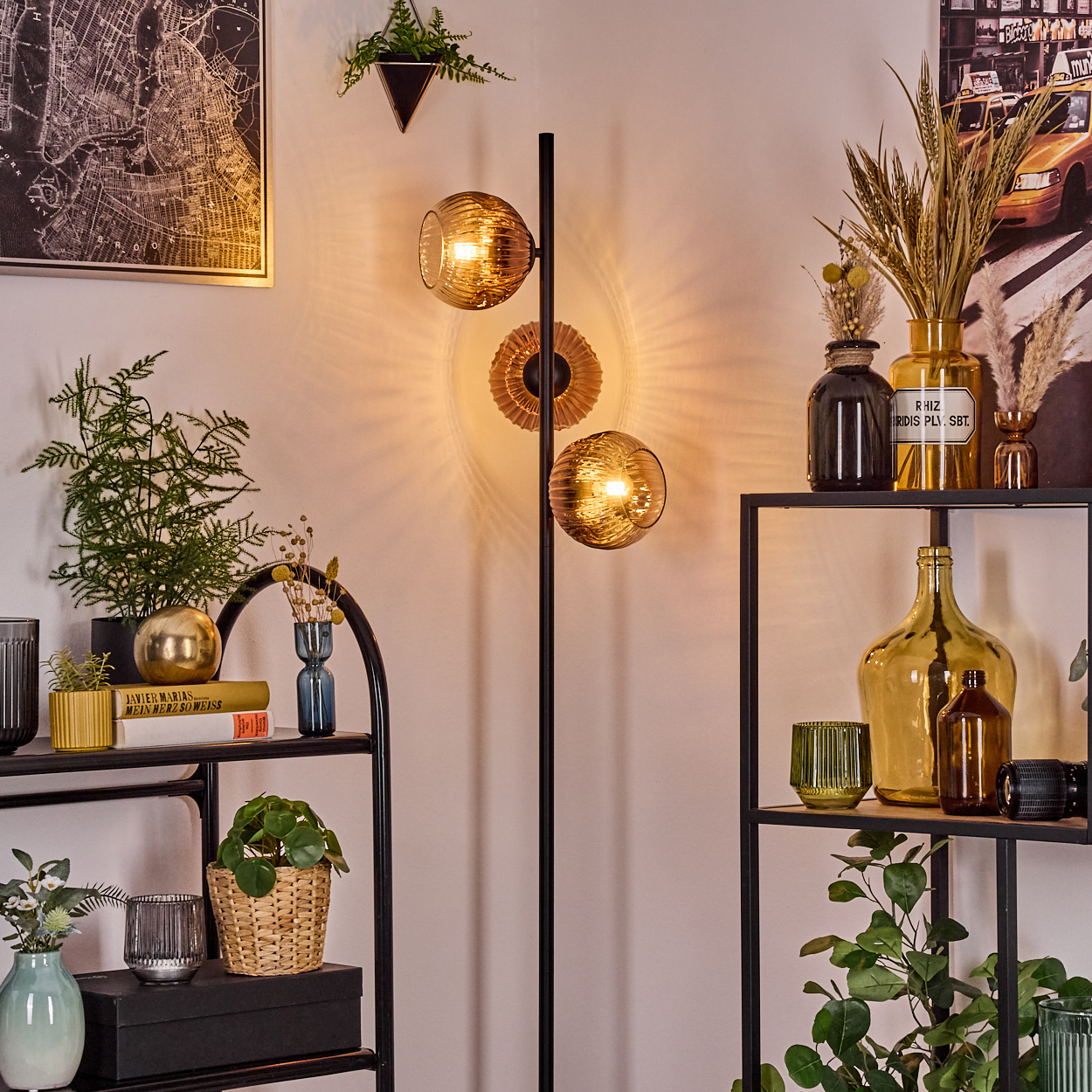 Ein Raum mit einer Stehlampe mit drei Glaskugeln. Regale mit Pflanzen, Vasen und Büchern. Eine Karte und ein Bild an der Wand.
