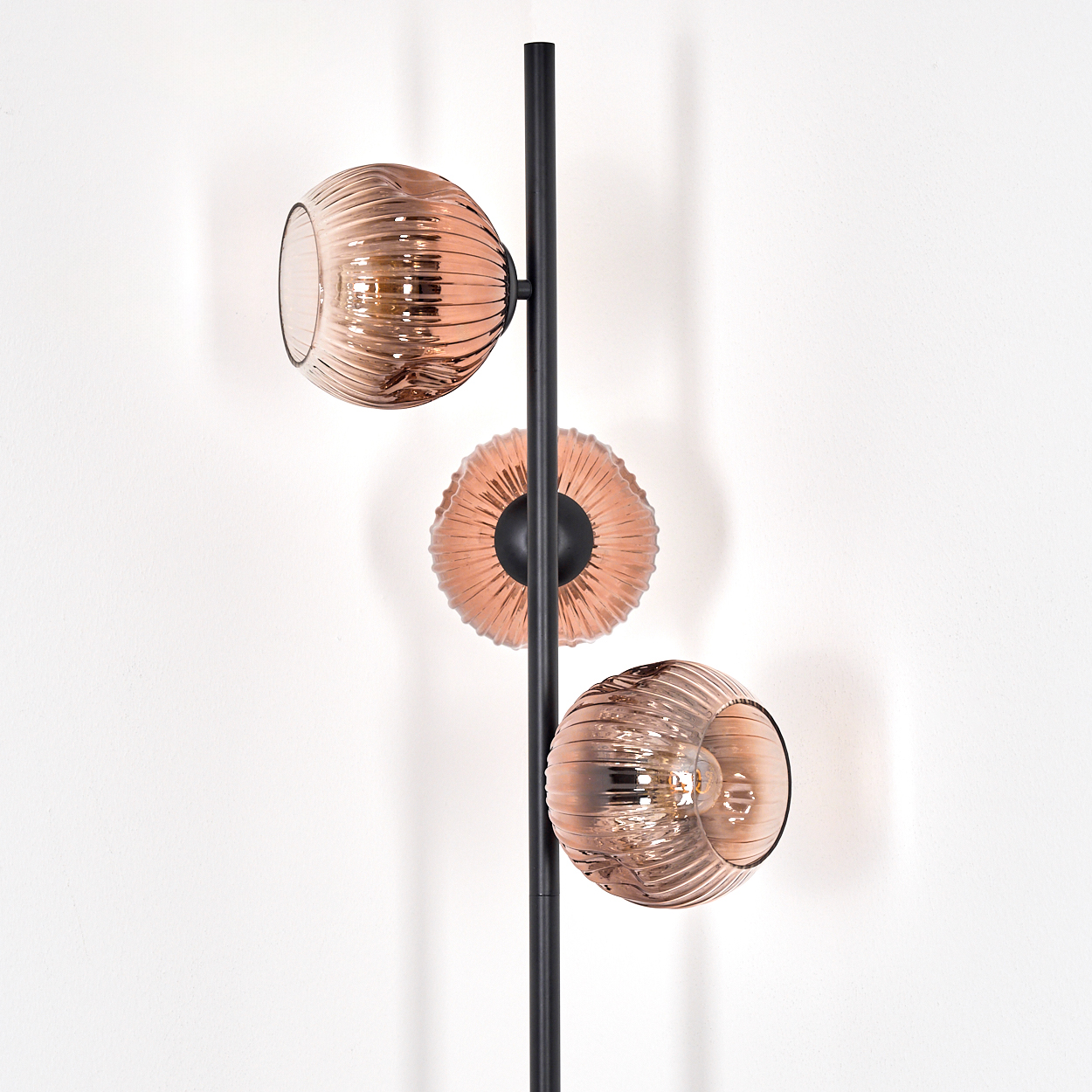 Eine moderne Lampe mit drei kupferfarbenen Glasschirmen, die an einer schwarzen Stange an einer weißen Wand befestigt sind.