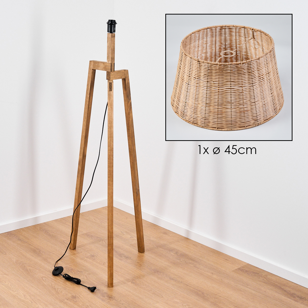 Holz-Dreibein-Lampe mit einem Korbschirmen. Ein schwarzes Kabel führt zum Boden, wo sich ein Schalter und ein Stecker befinden.